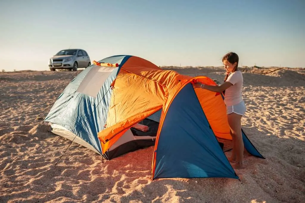 Girl setting up tent on beach to beach camp.