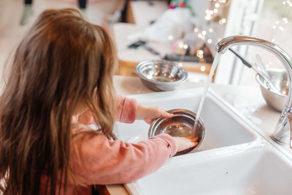Little girl washing dishes in RV sink.
