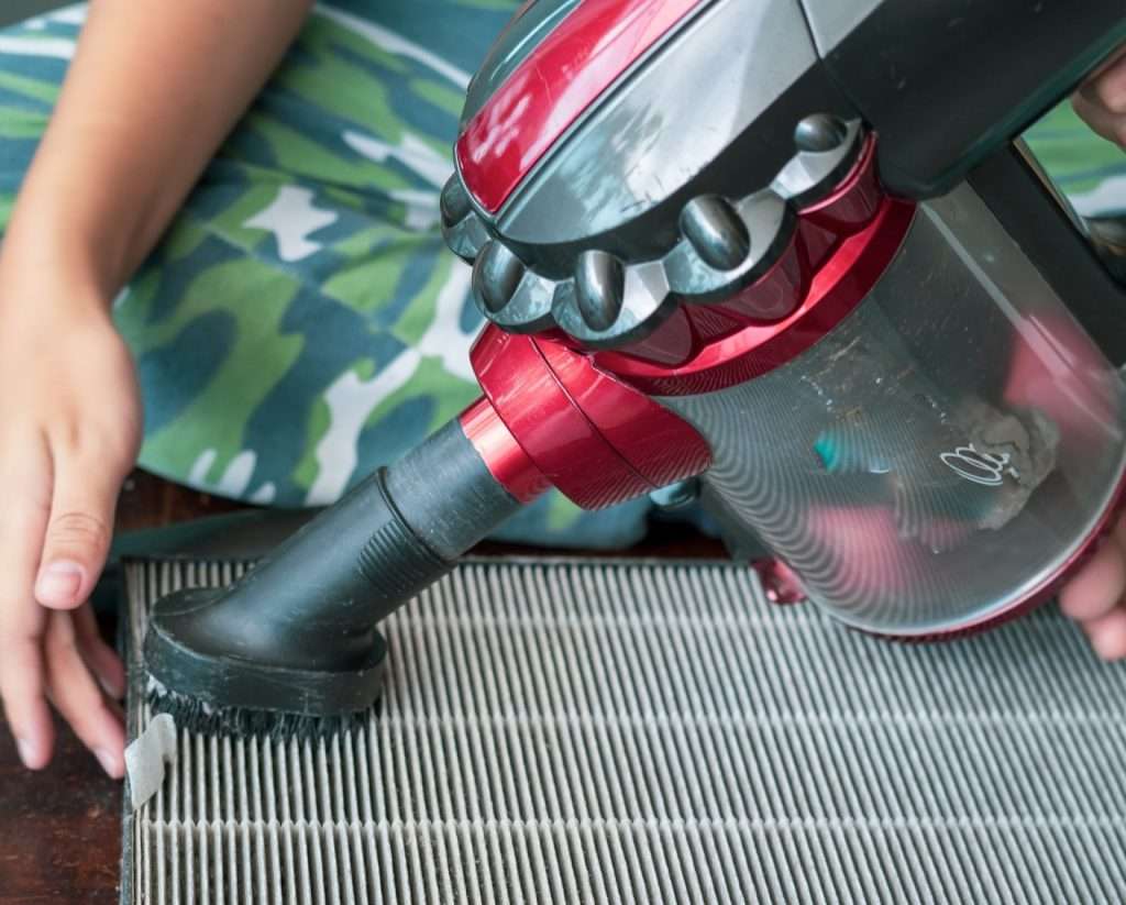 Woman using a hand vacuum on vent.
