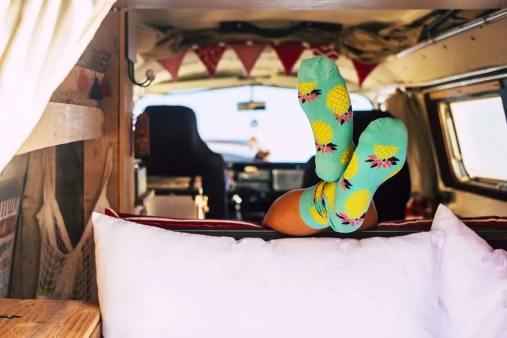 Travel lifestyle with minivan and vanlife style - unrecognizable girl inside a retro camper - feet with socks visible from a lay down unrecognizable people