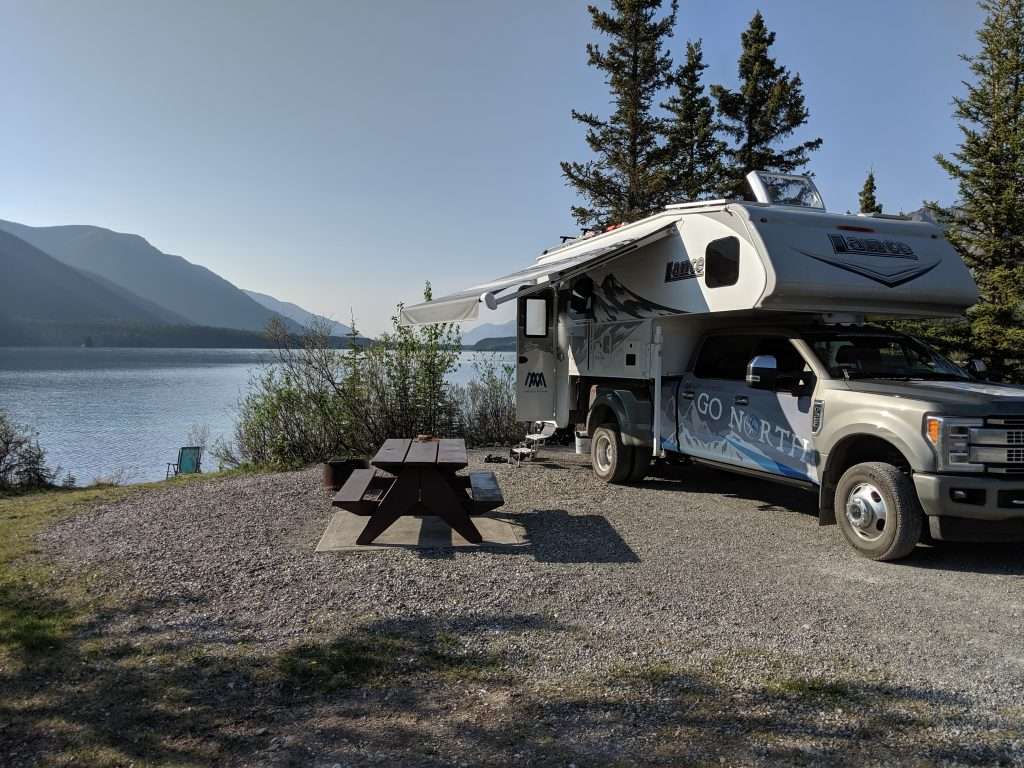 Go North truck camper parked by scenic lake with awning open.