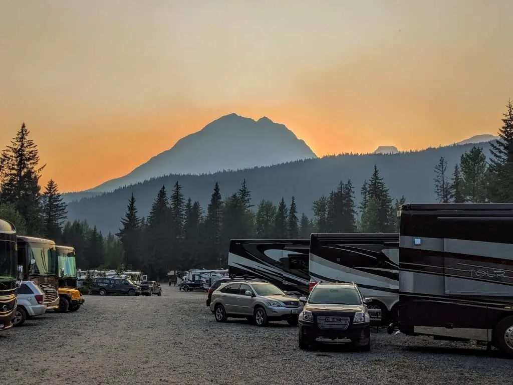 Crowded RV parking lot in front of mountain at sunset.