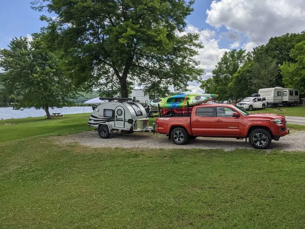 Truck and travel camper parked in campsite by water.