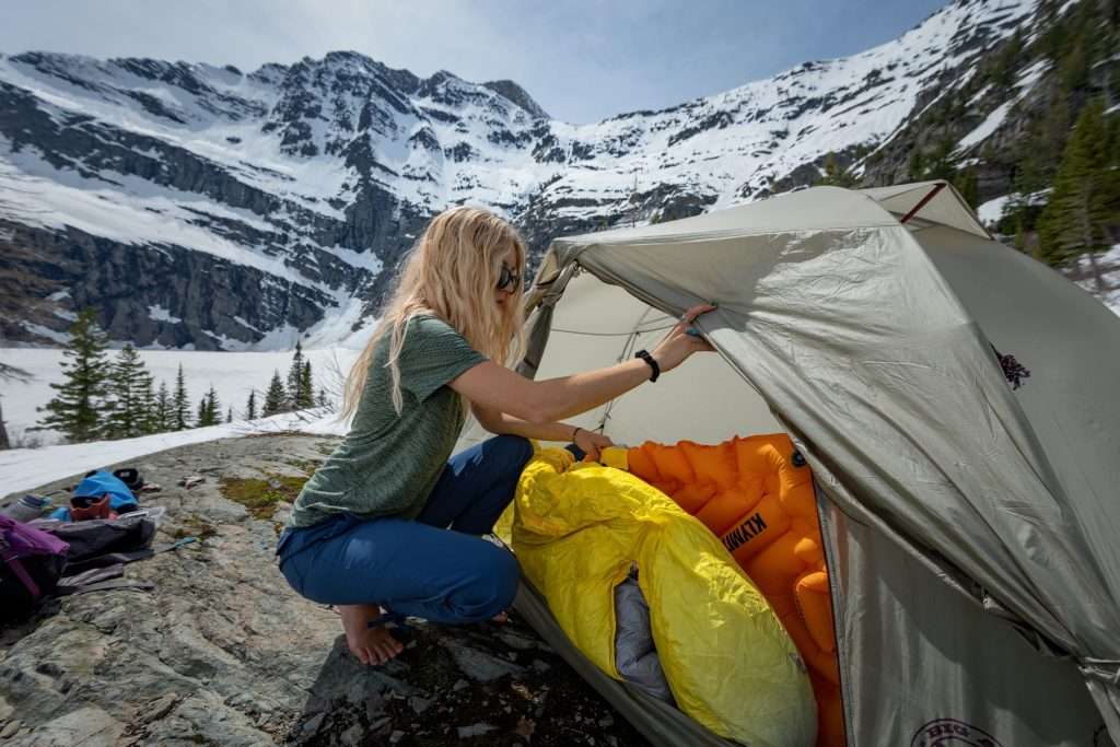 Woman setting up sleeping bag on a snowy mountain.