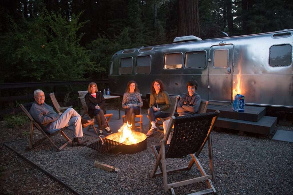 Family around campfire in front of airstream.