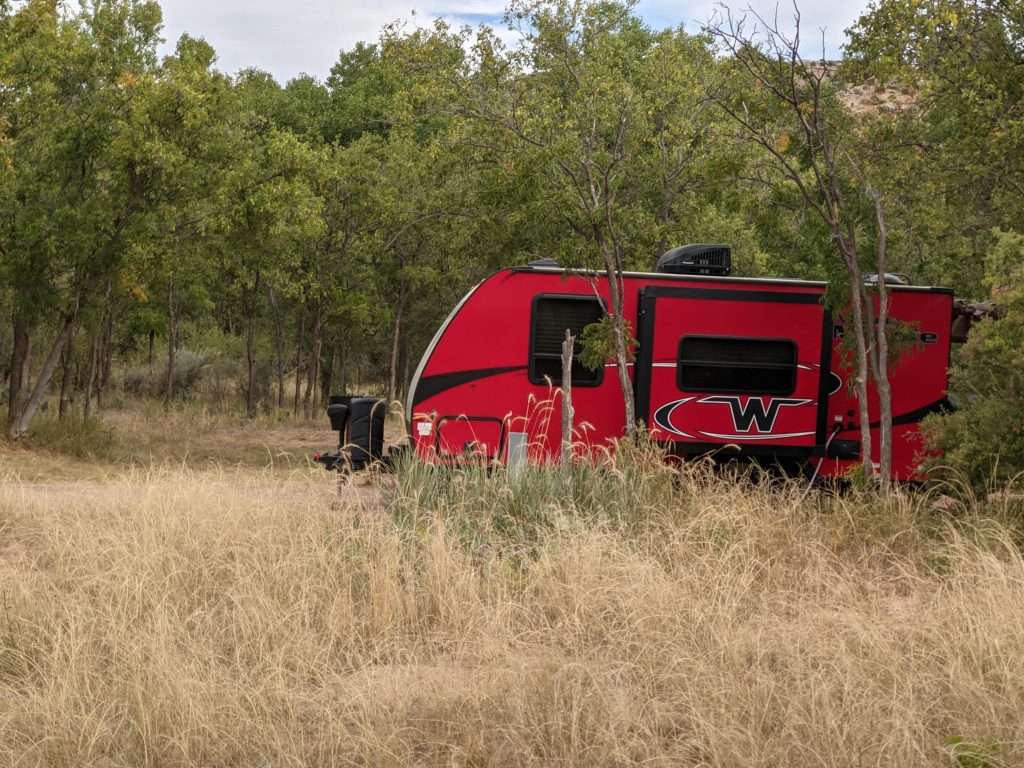 Red trailer parked in between trees for boondocking.