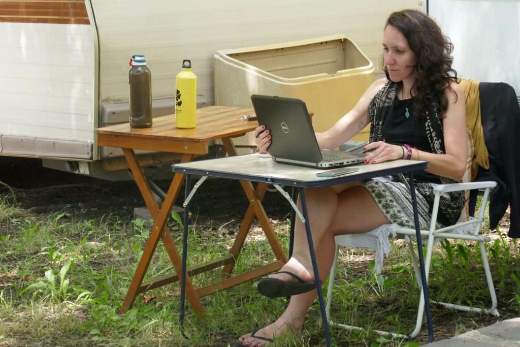 Woman working on laptop in front of RV on foldable table.