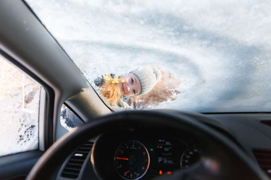 Kid peeking through snowy car window.