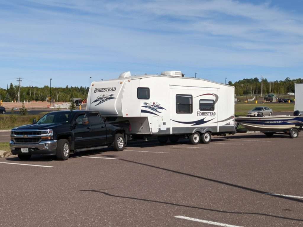 Black truck double towing 5th wheel and boat.