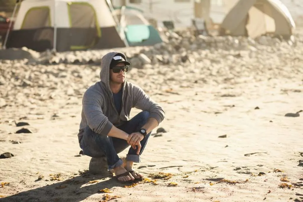 Man sitting next to tent on beach.