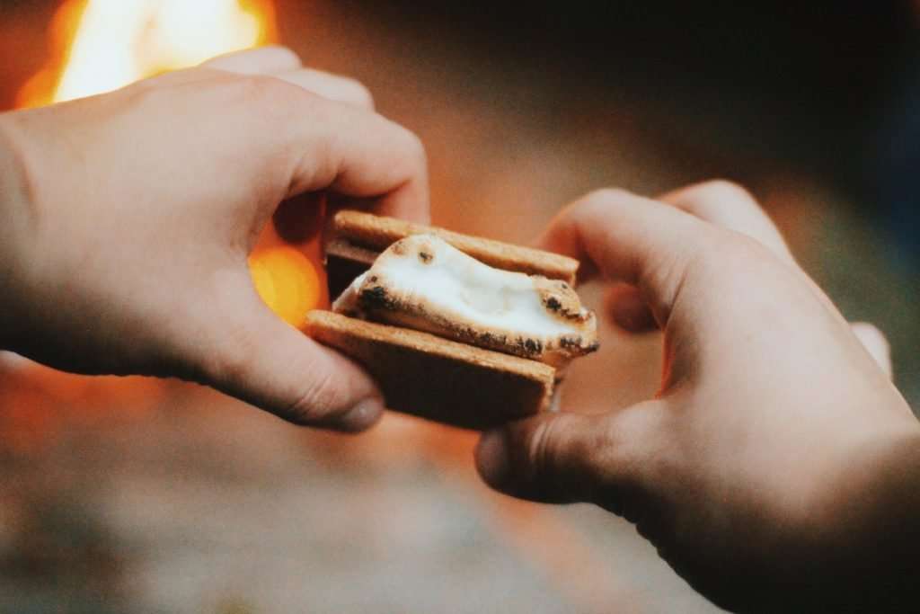 Hands holding a s'more by the fire.