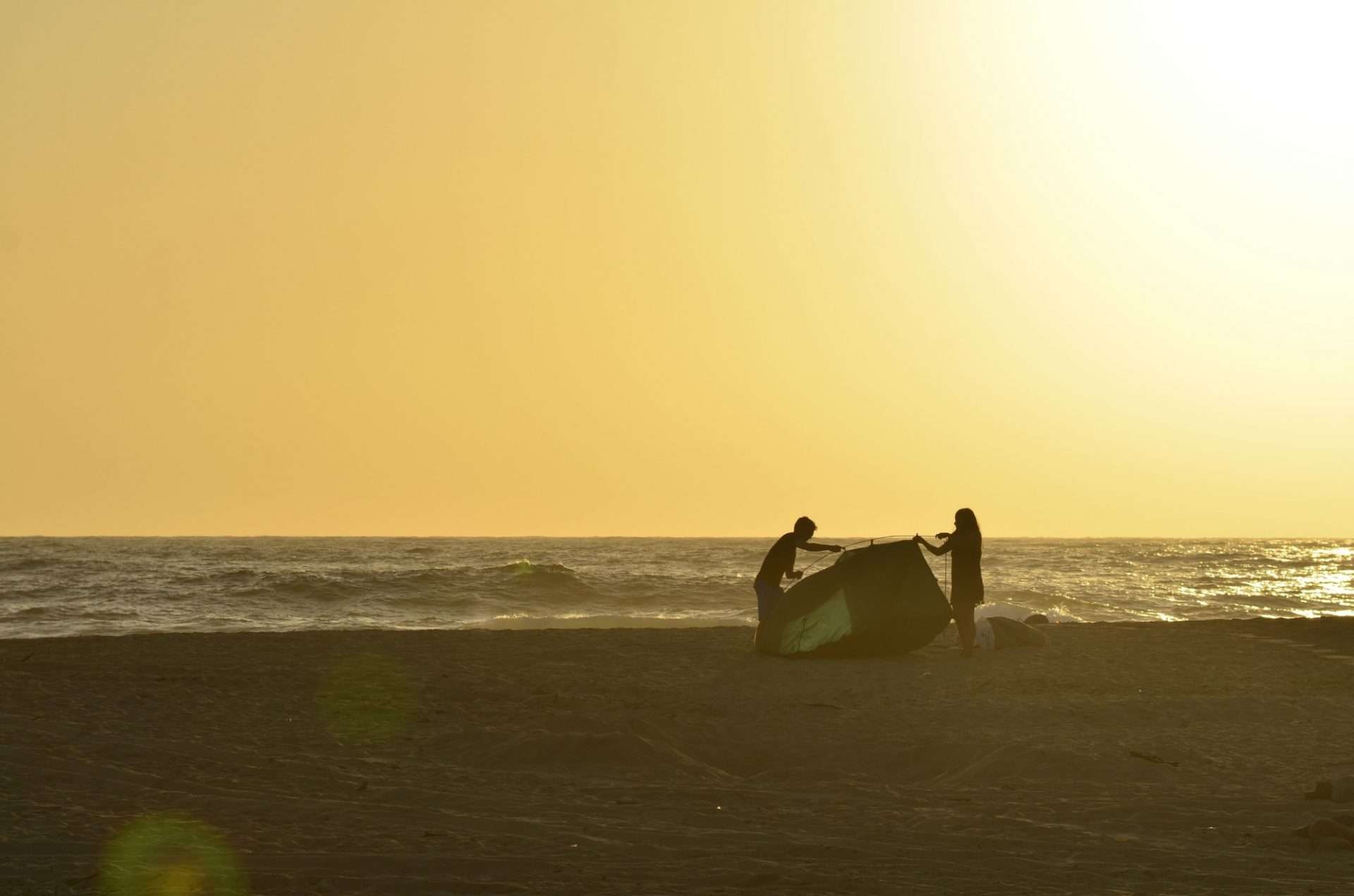 Couple putting tent together on California beach at sunset.