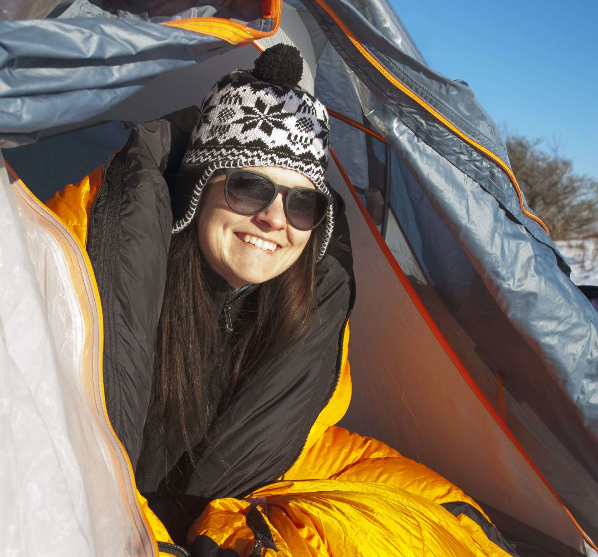 Woman looking out of tent flap smiling wearing winter hat.