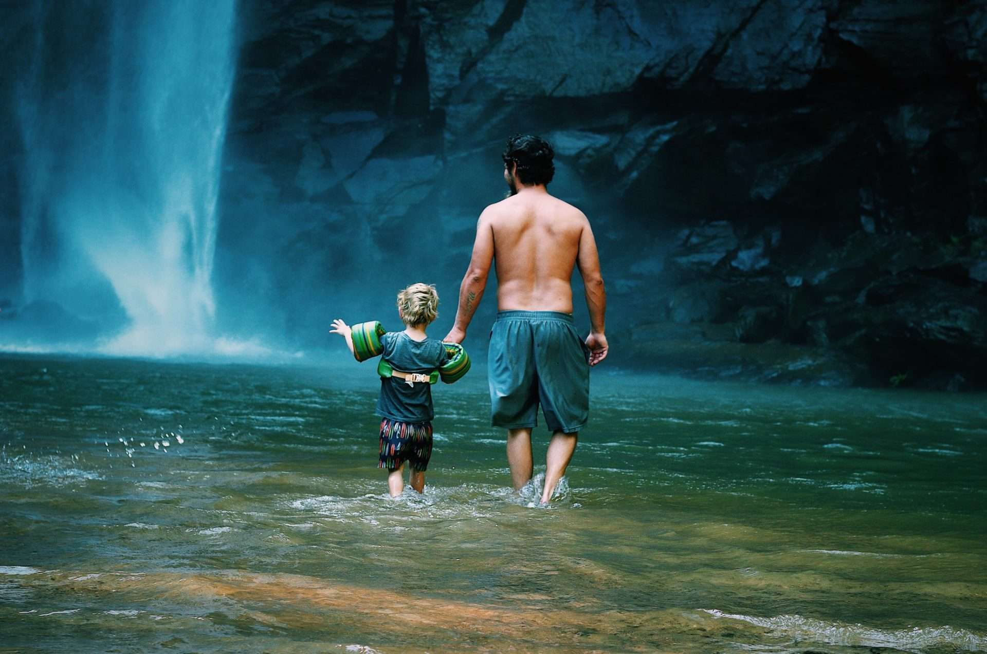 Dad and son walking into waterfall. 