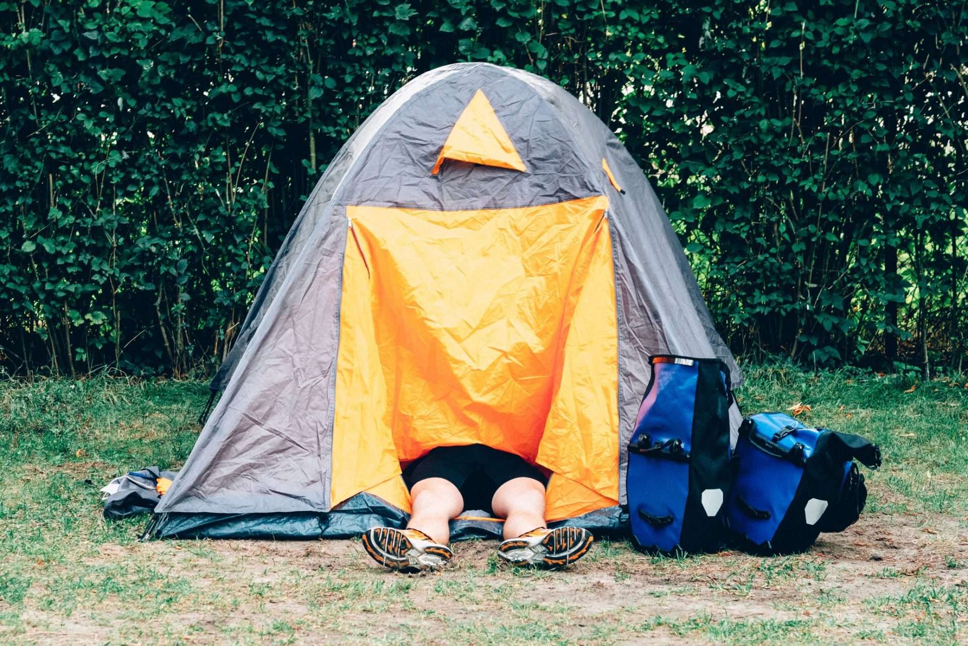 Man laying with legs out of tent because he is too tall.