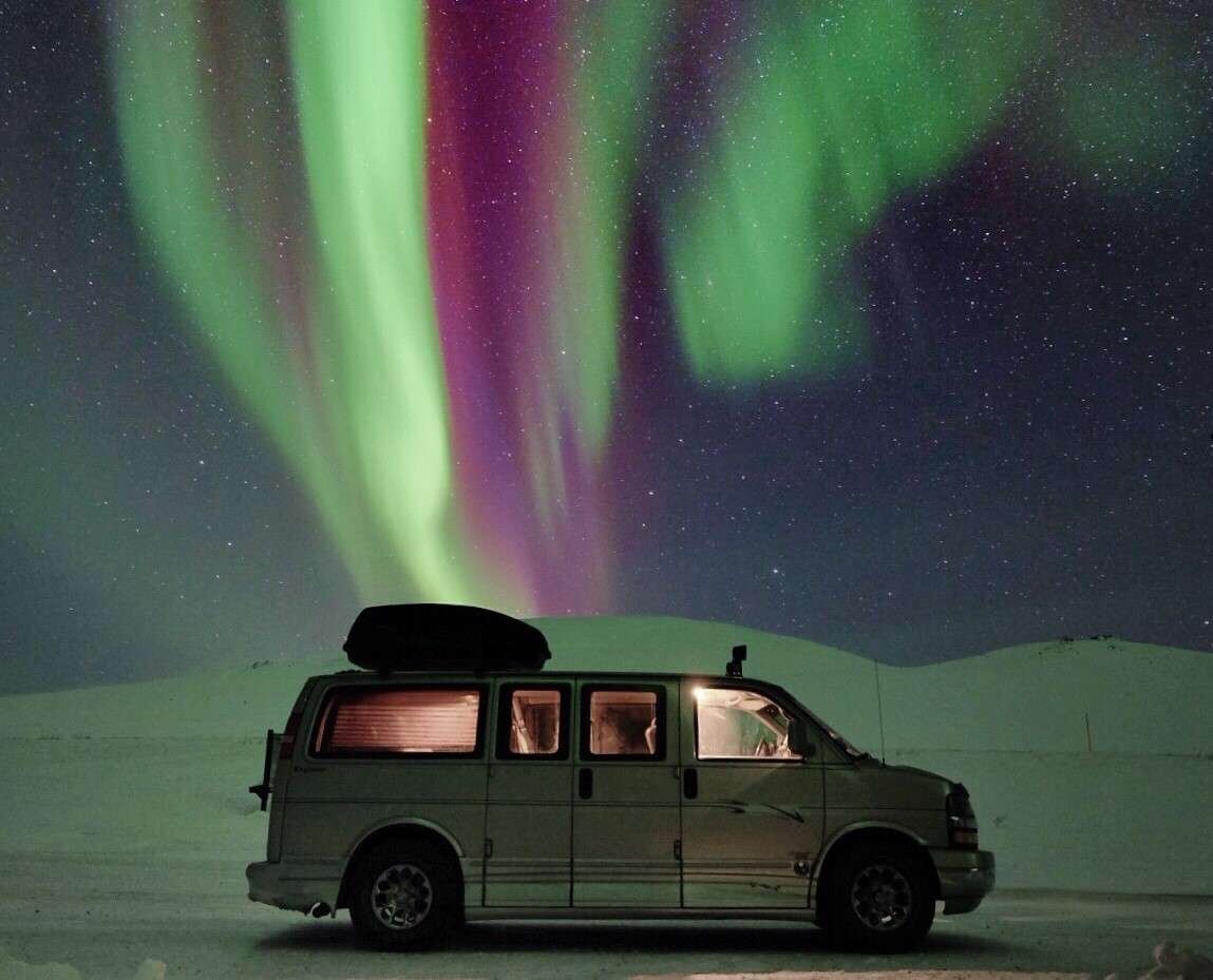 Camper van driving in front of Northern Lights. 