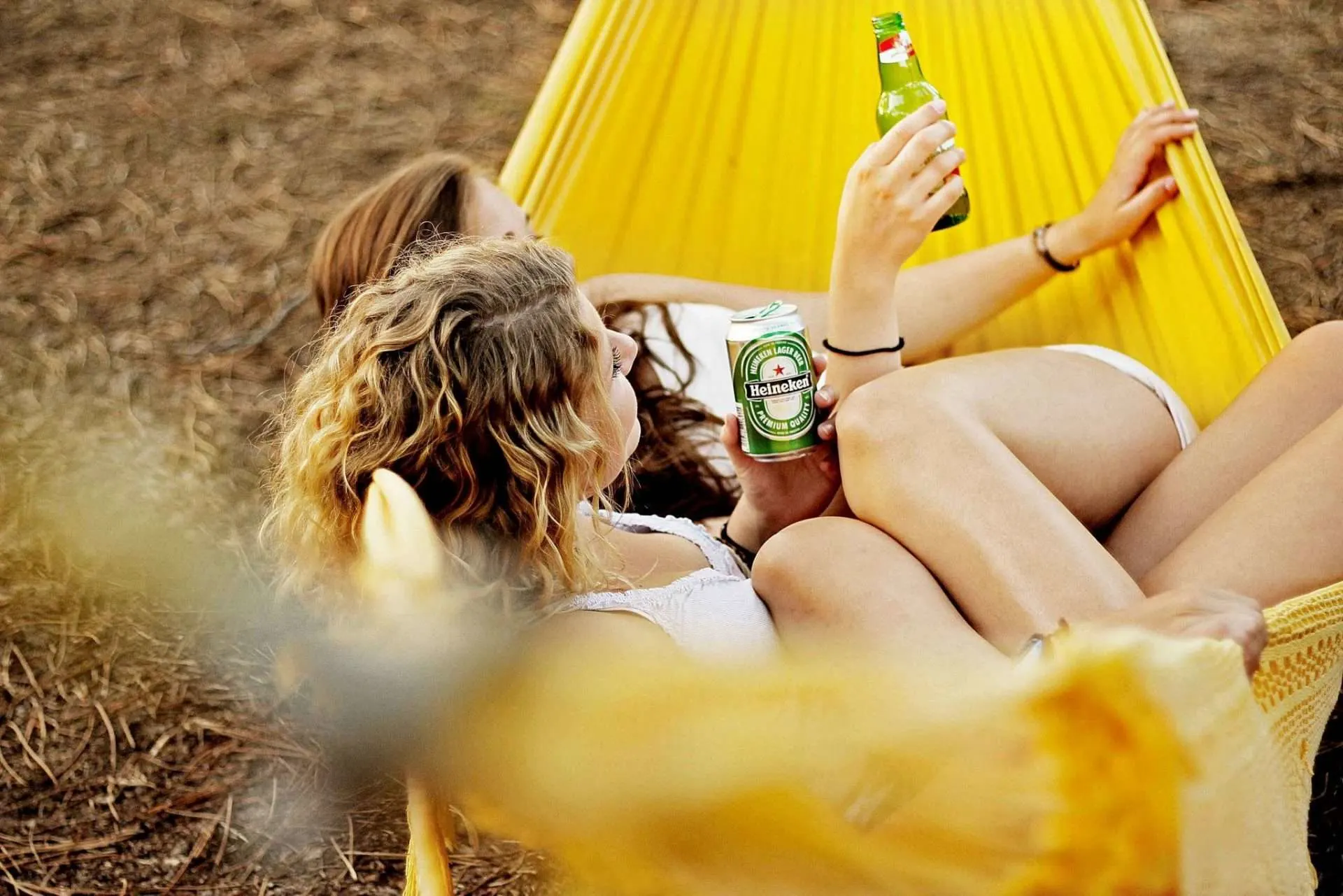 Two friends drinking beer in free-standing yellow hammock.