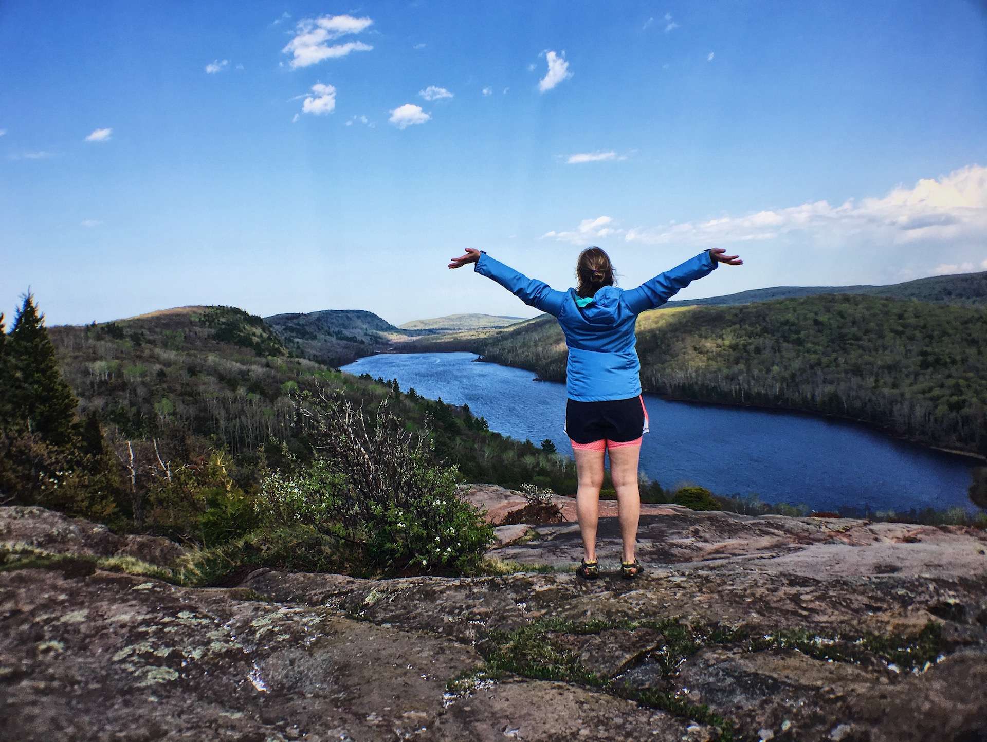 woman with arms raised with lake of the clouds in distance at porcupine mountains state park in michigan