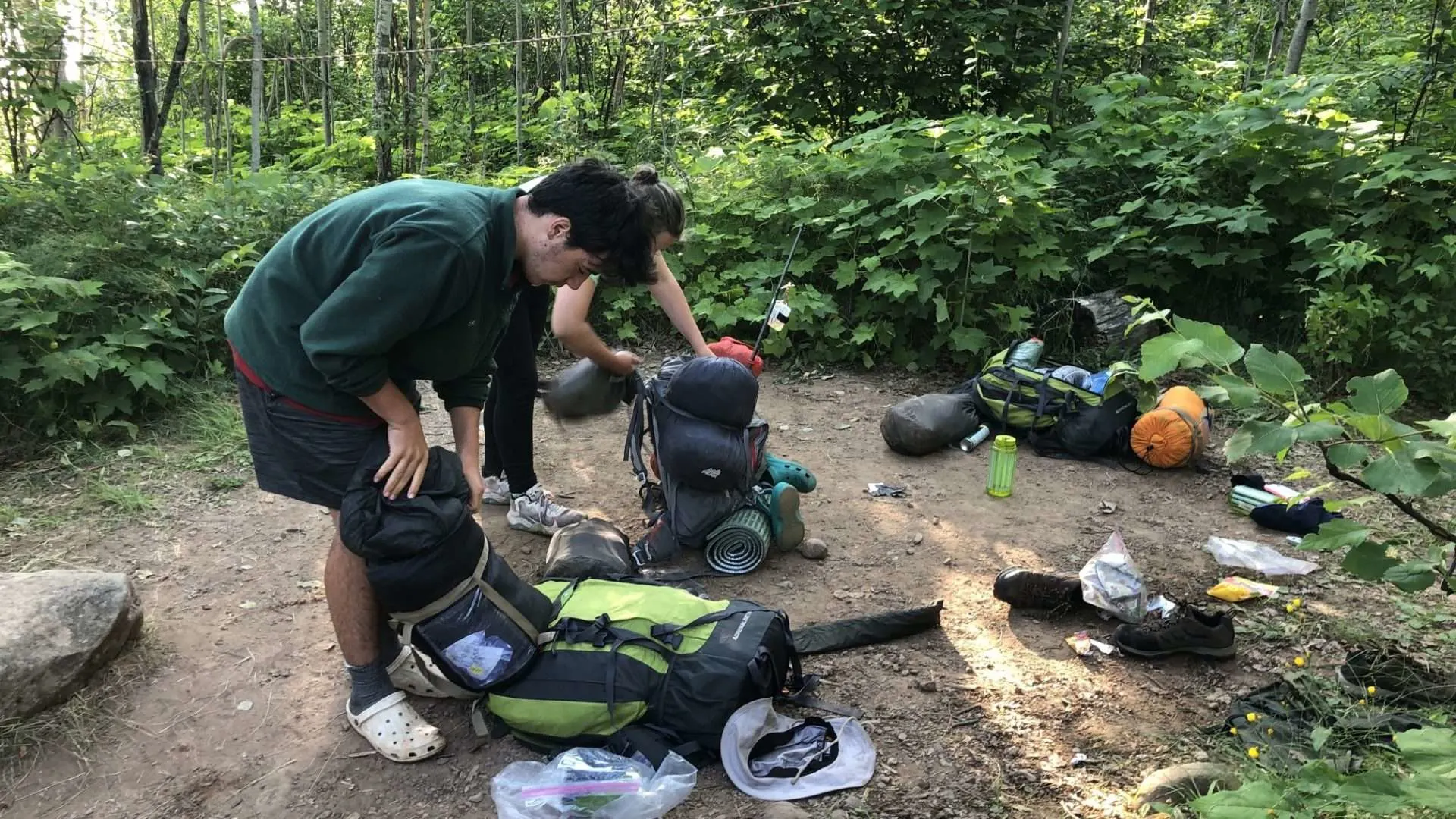 Couple unpacking heavy camping bags at campsite.