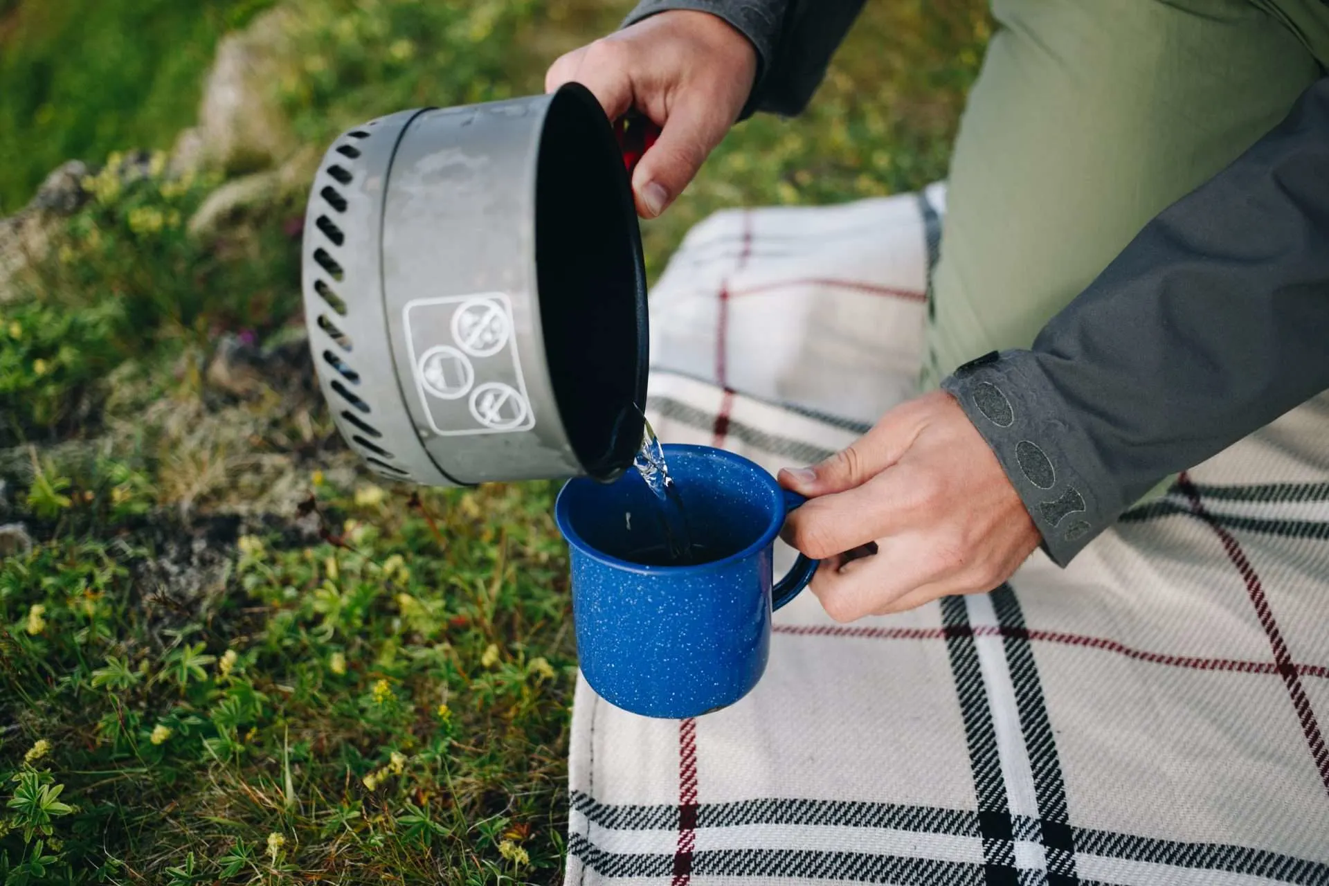 Person pouring boiled water from pot into cup while camping.