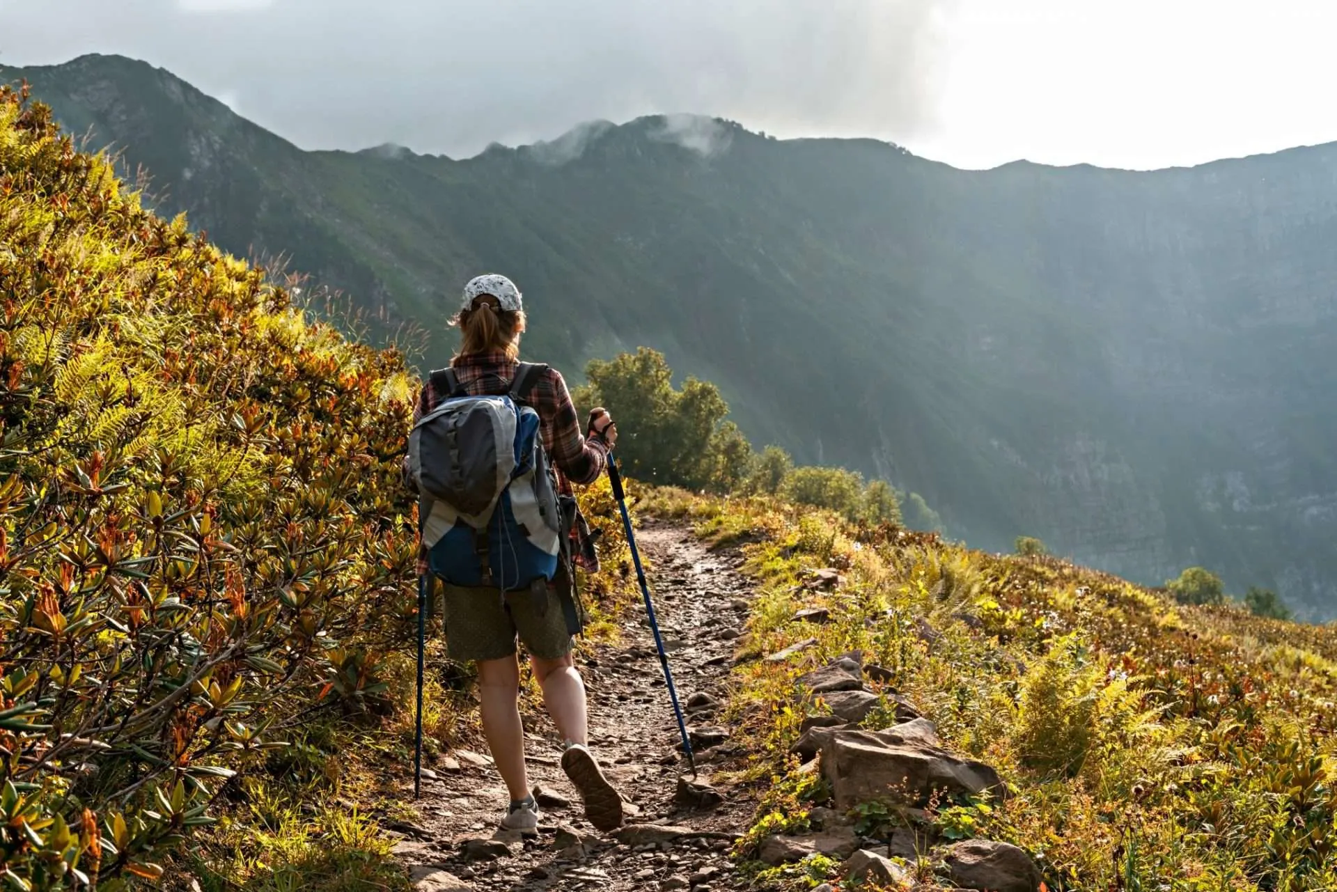 Woman hiking with walking sticks through scenic mountains.