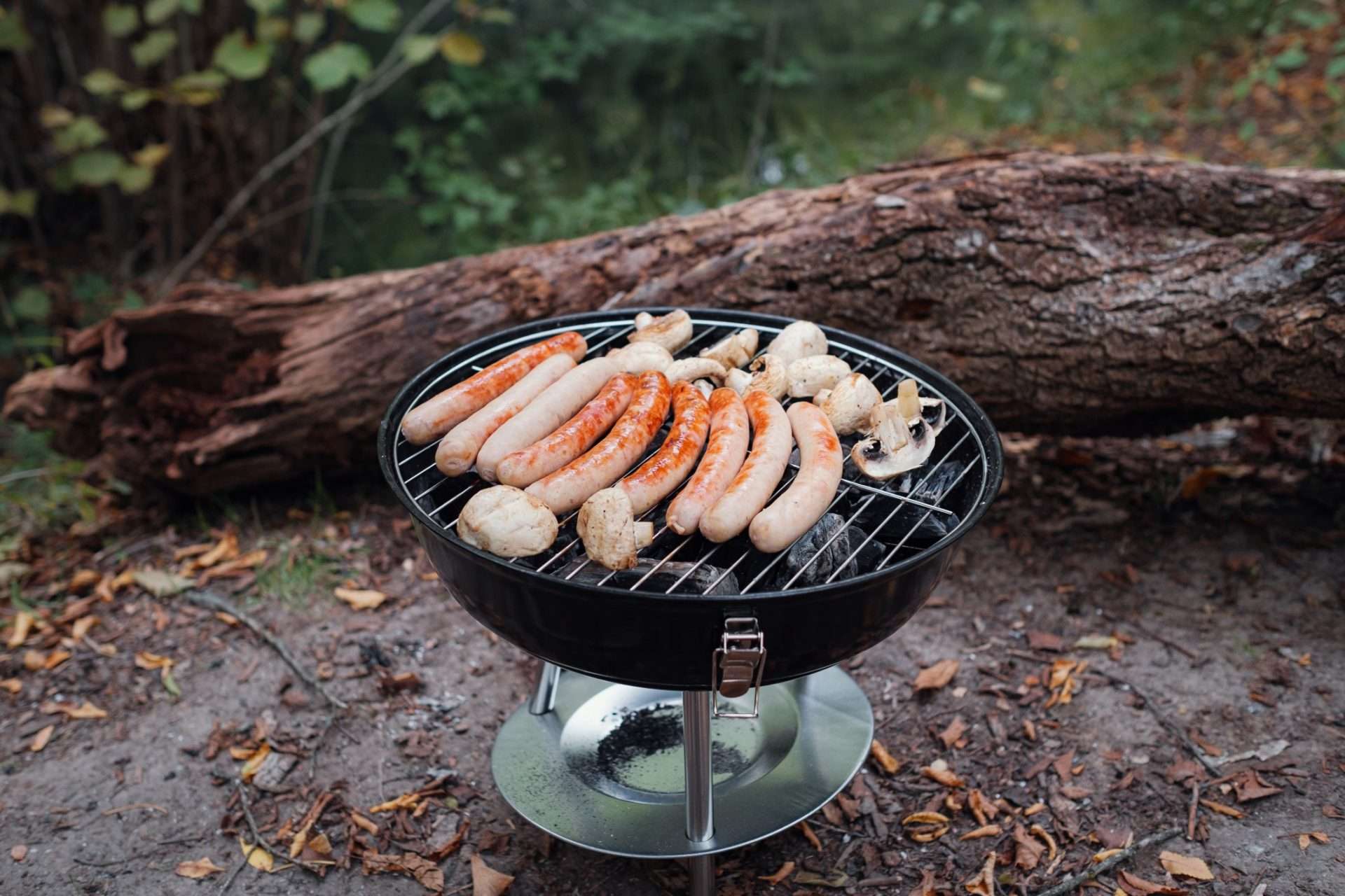 Bratwursts and mushrooms being cooked on a portable grill.
