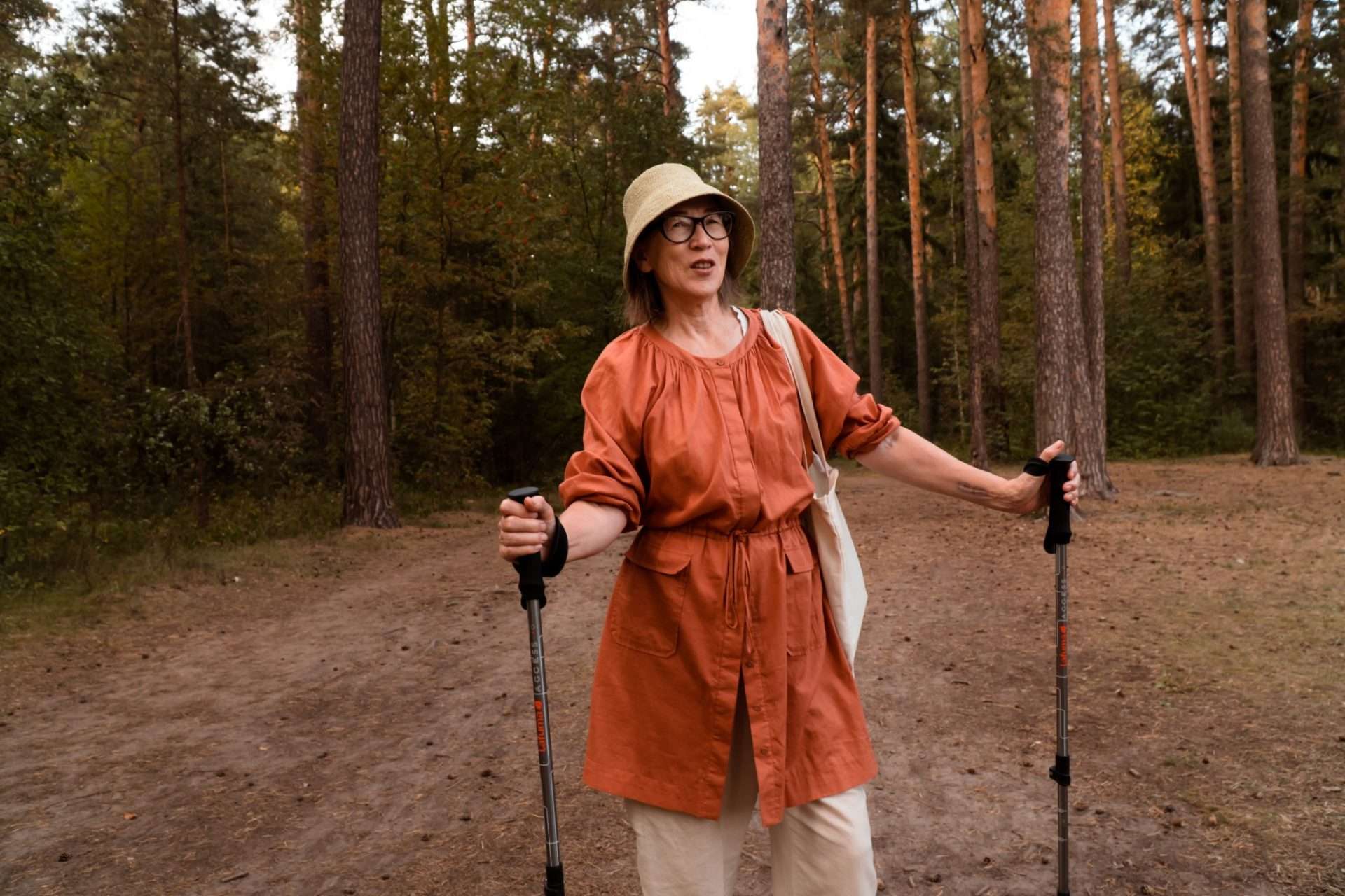 Older woman using trekking poles while hiking in forest.