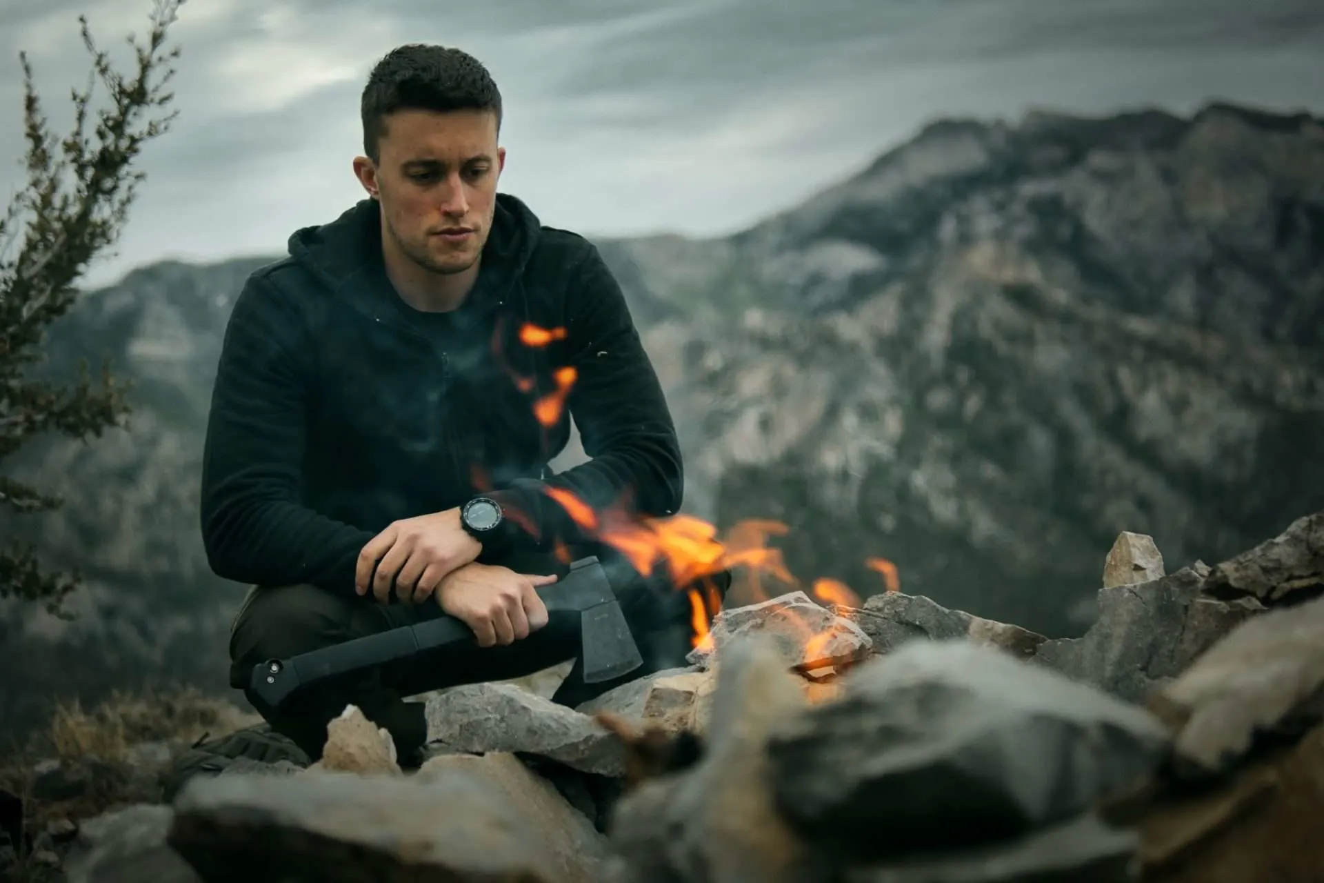 Male survivalist camper sitting by fire.