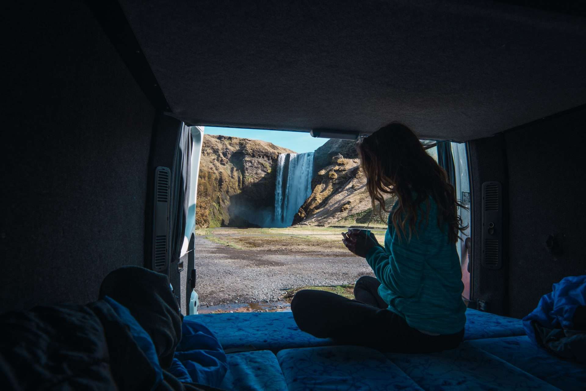 Woman looking at Icelandic waterfall from inside camper van rental