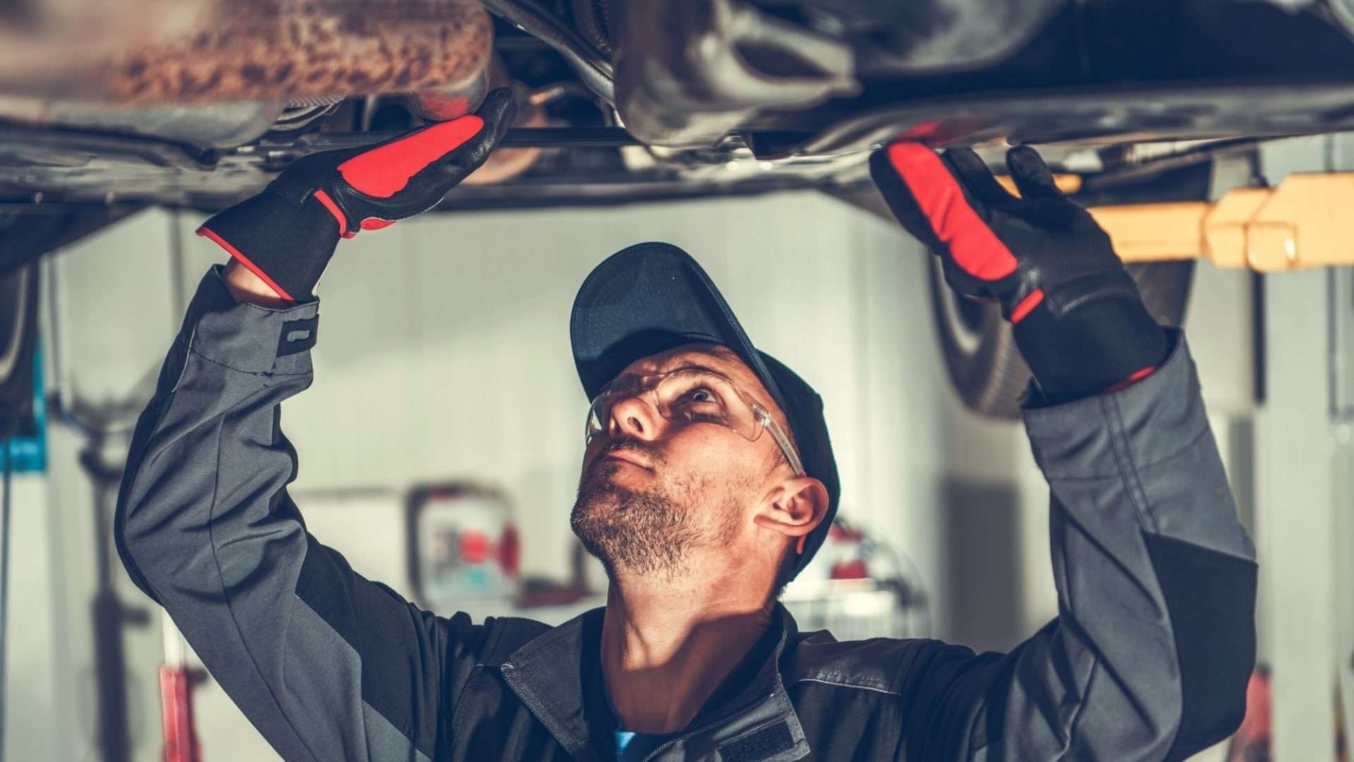 Mechanic removing rust from undercarriage of vehicle