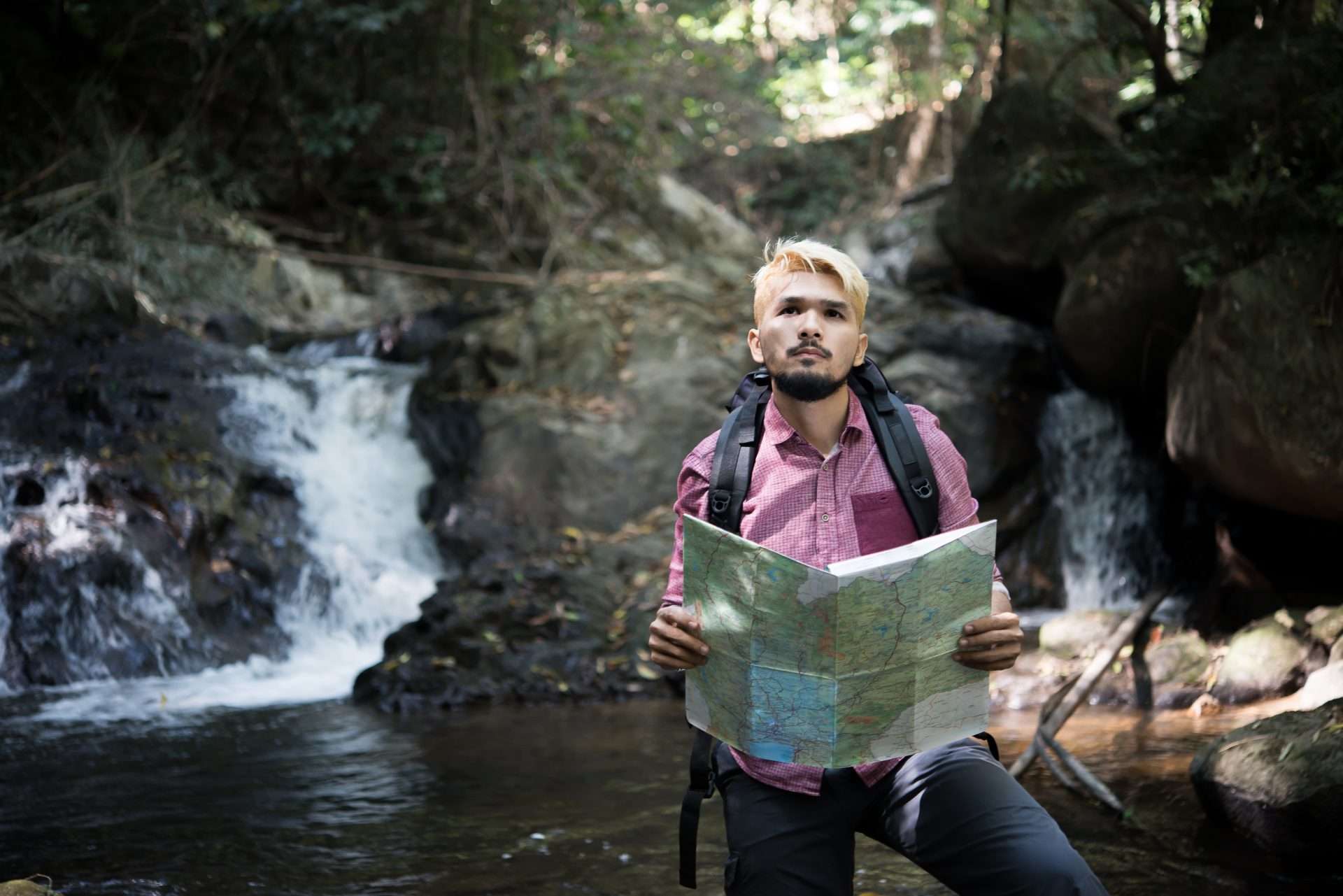 Man holding map by waterfall while hiking
