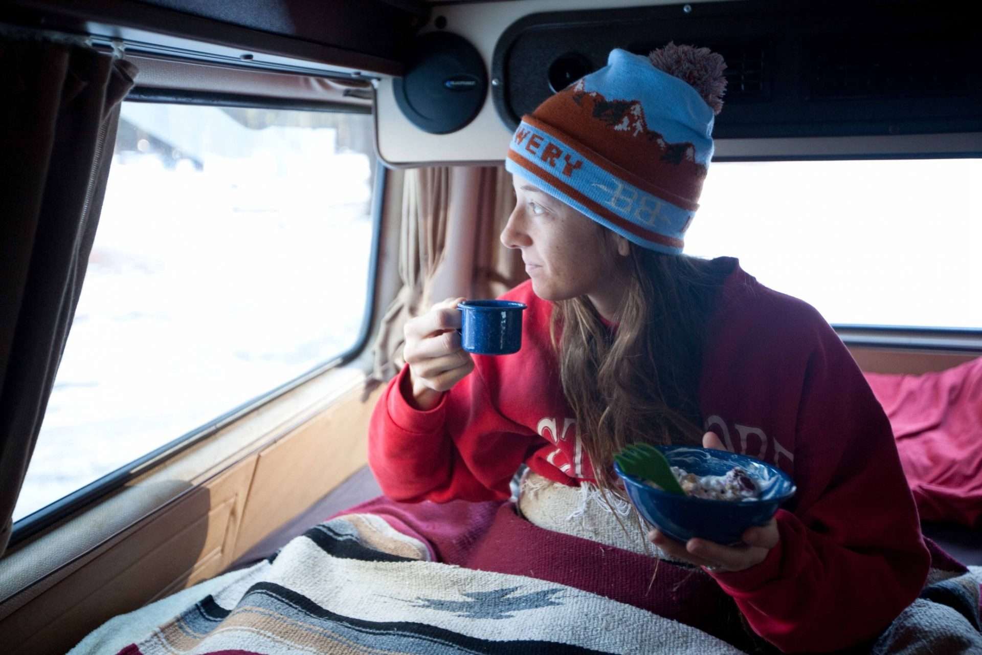 Woman drinking coffee and eating breakfast in camper van while stealth camping.