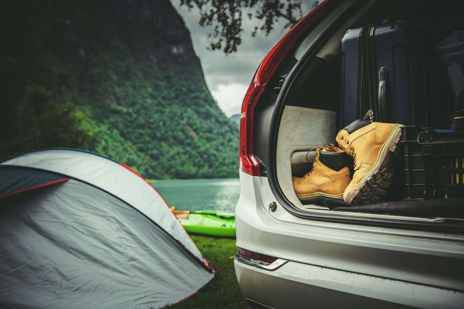 Tent set up by lake with camping gear in the back of a car