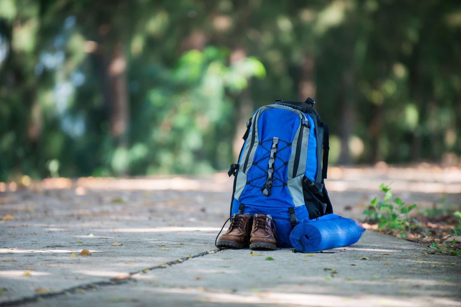 Daypack and hiking boots sitting on sidewalk.