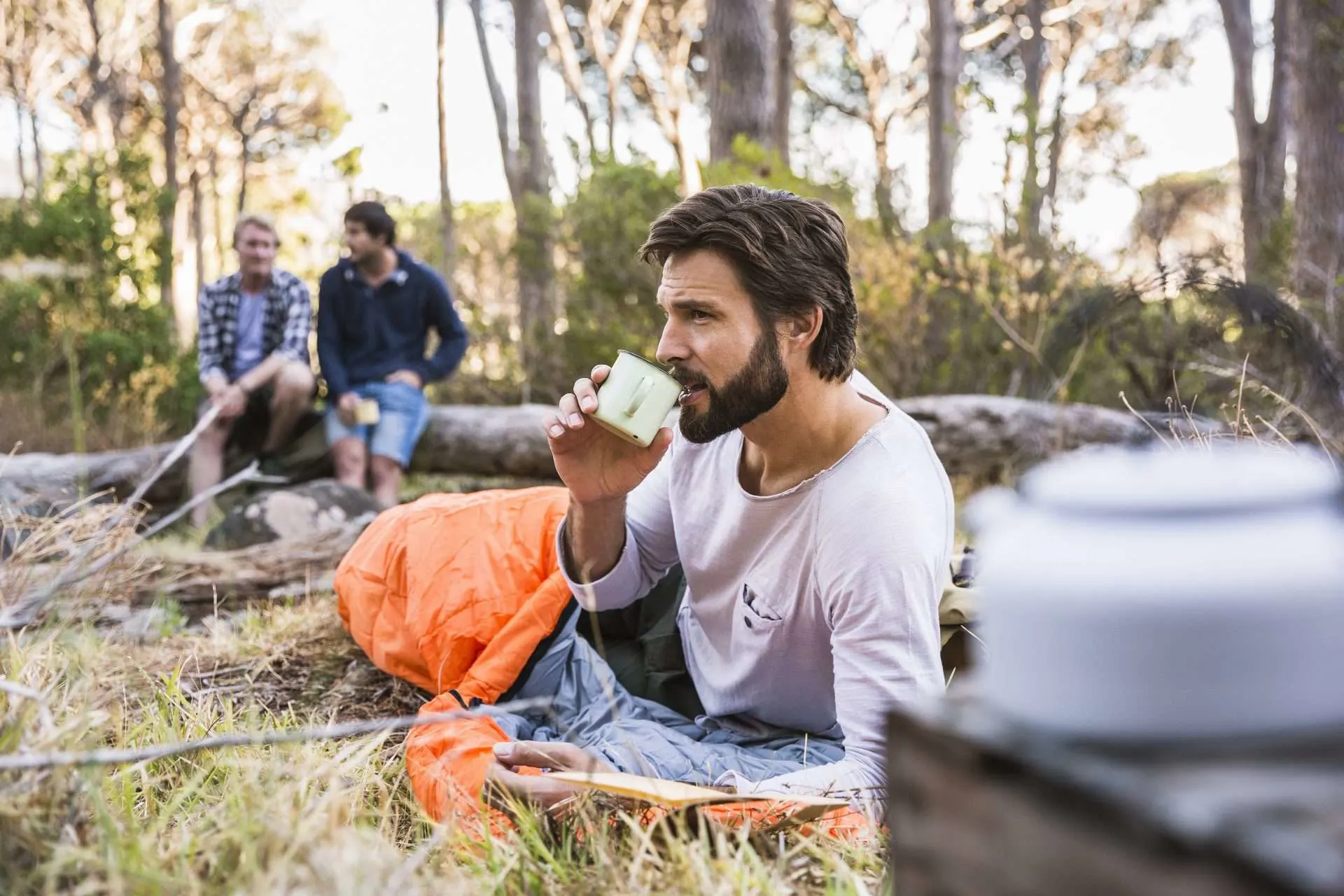 Man drinking coffee in sleeping bag while camping.