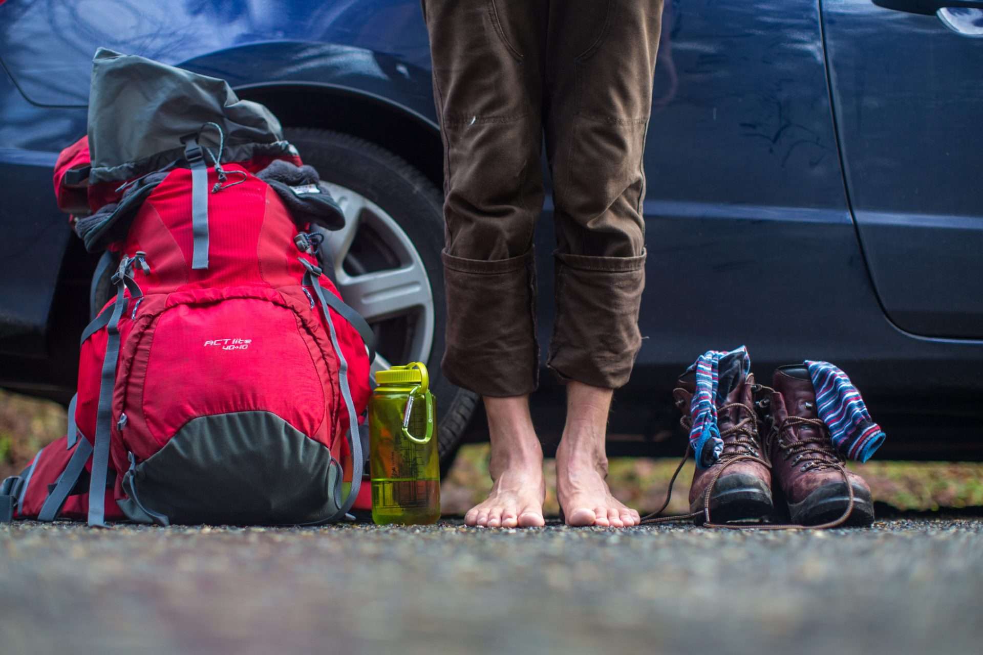 Person standing barefoot in front of hiking backpack and boots and socks
