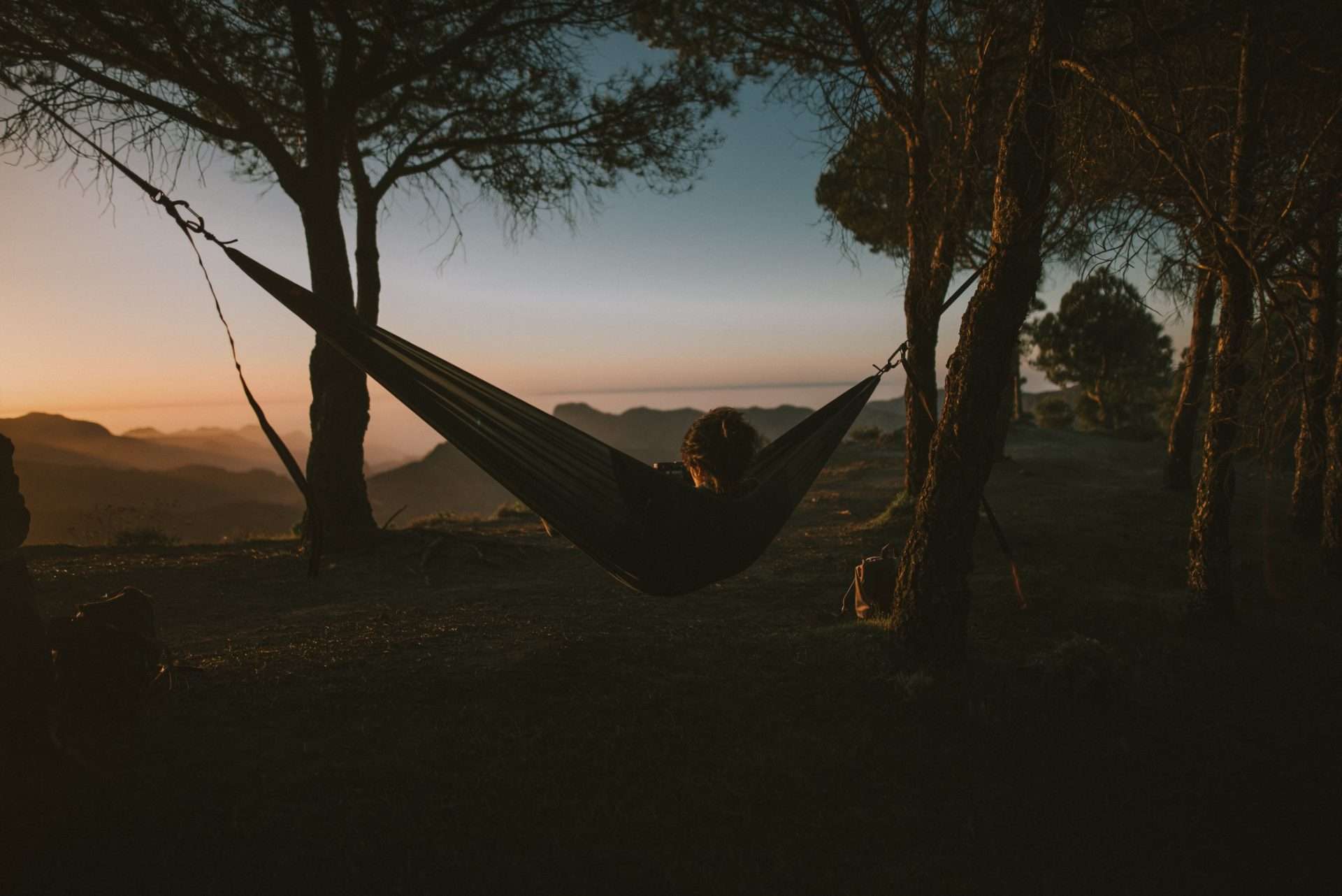Person sleeping in a hammock while the sun sets