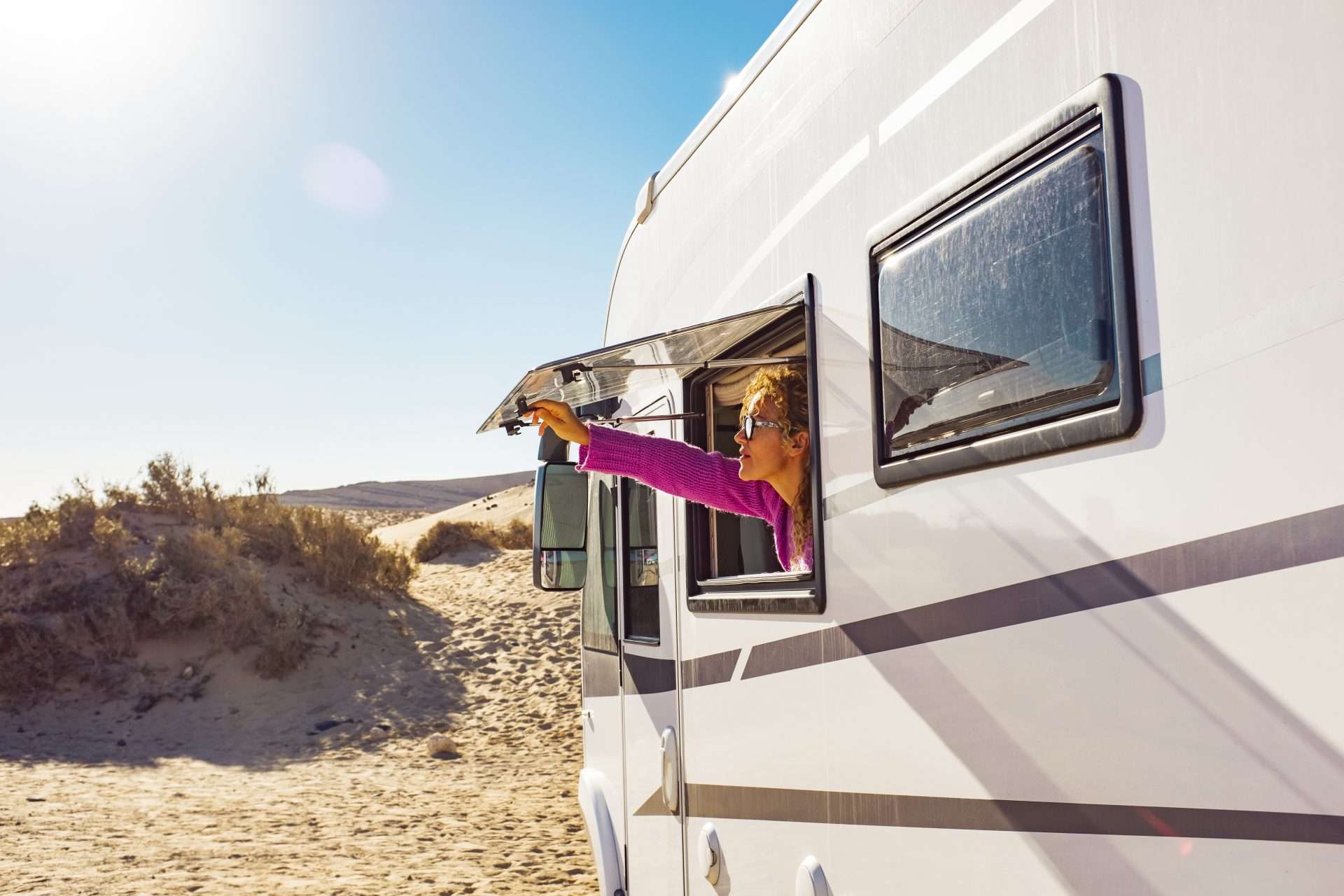 Woman looking out window of RV at ocean while RV beach camping.