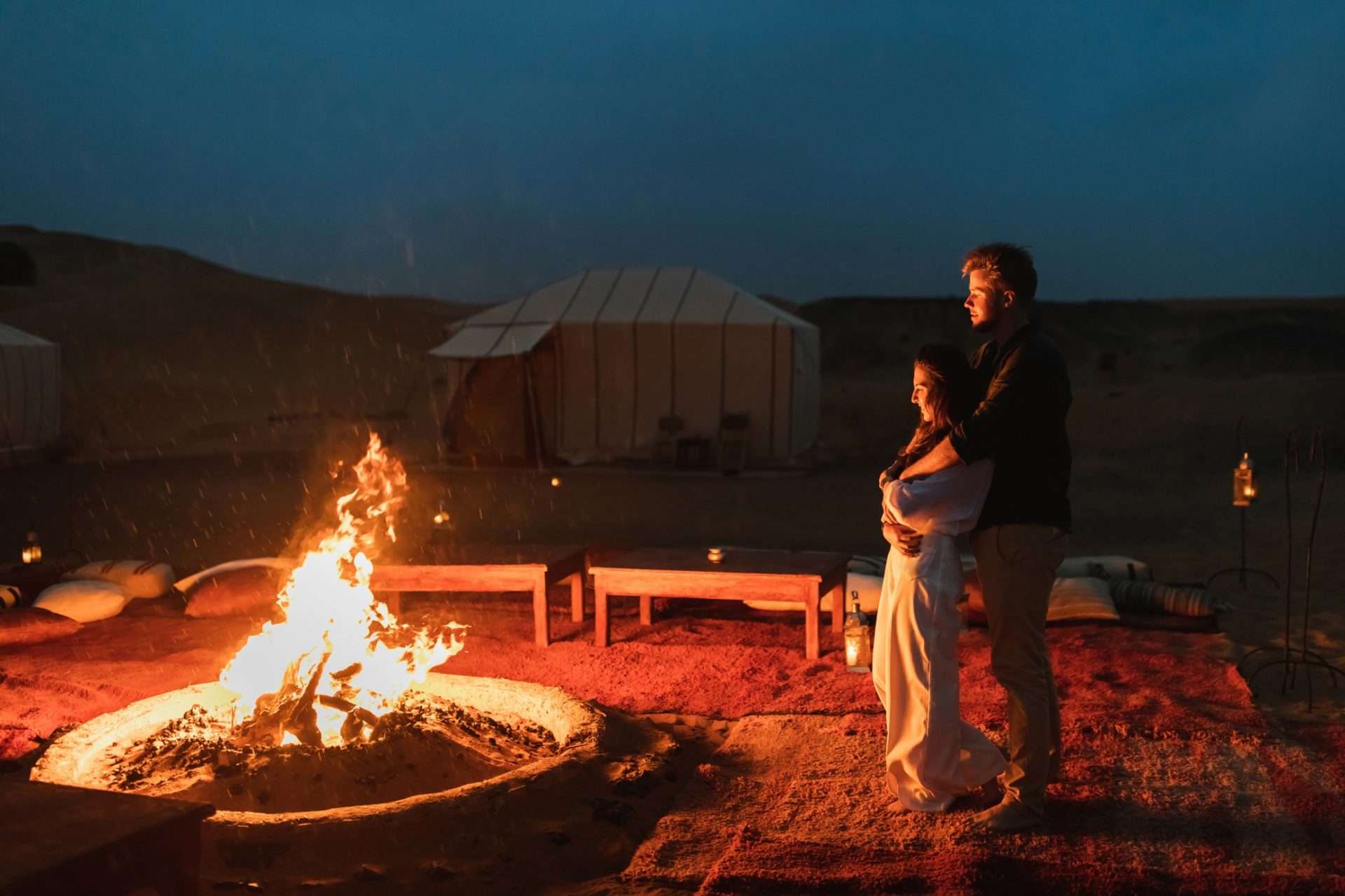Couple standing in front of campfire and yurt in Joshua Tree