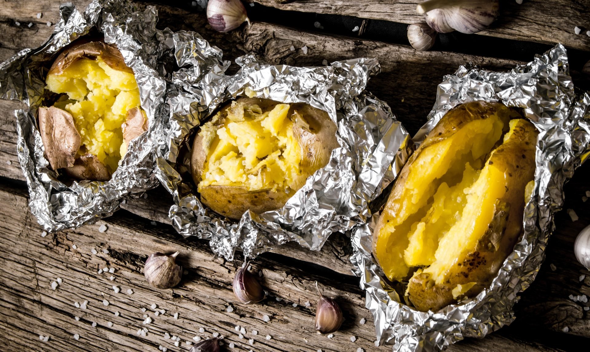 Three baked potatoes wrapped in foil on picnic table