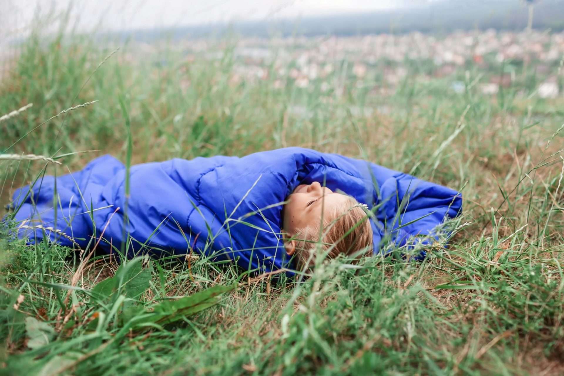 Boy sleeping in sleeping bag in big grass field while cowboy camping