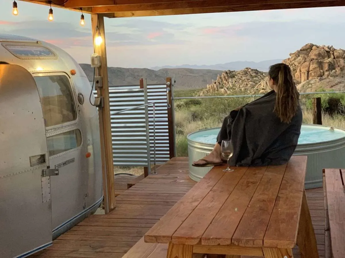 Woman drinking a glass of wine next to Airstream glamping site in Joshua Tree