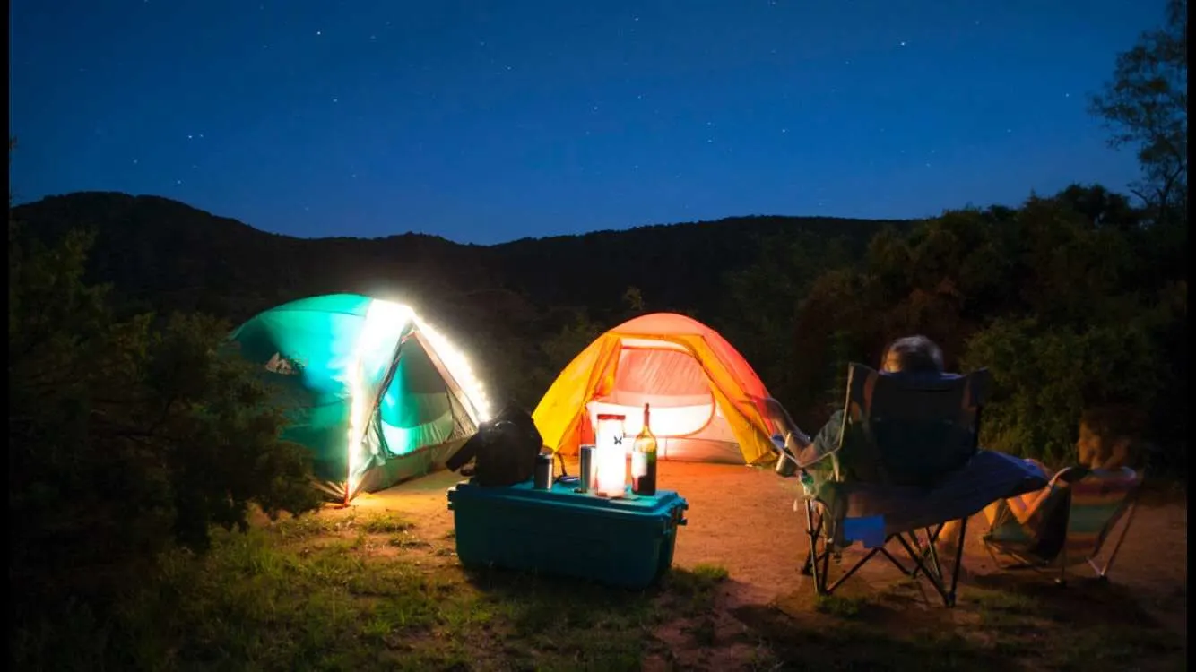 Two tents set up at campsite at night with camping cooler