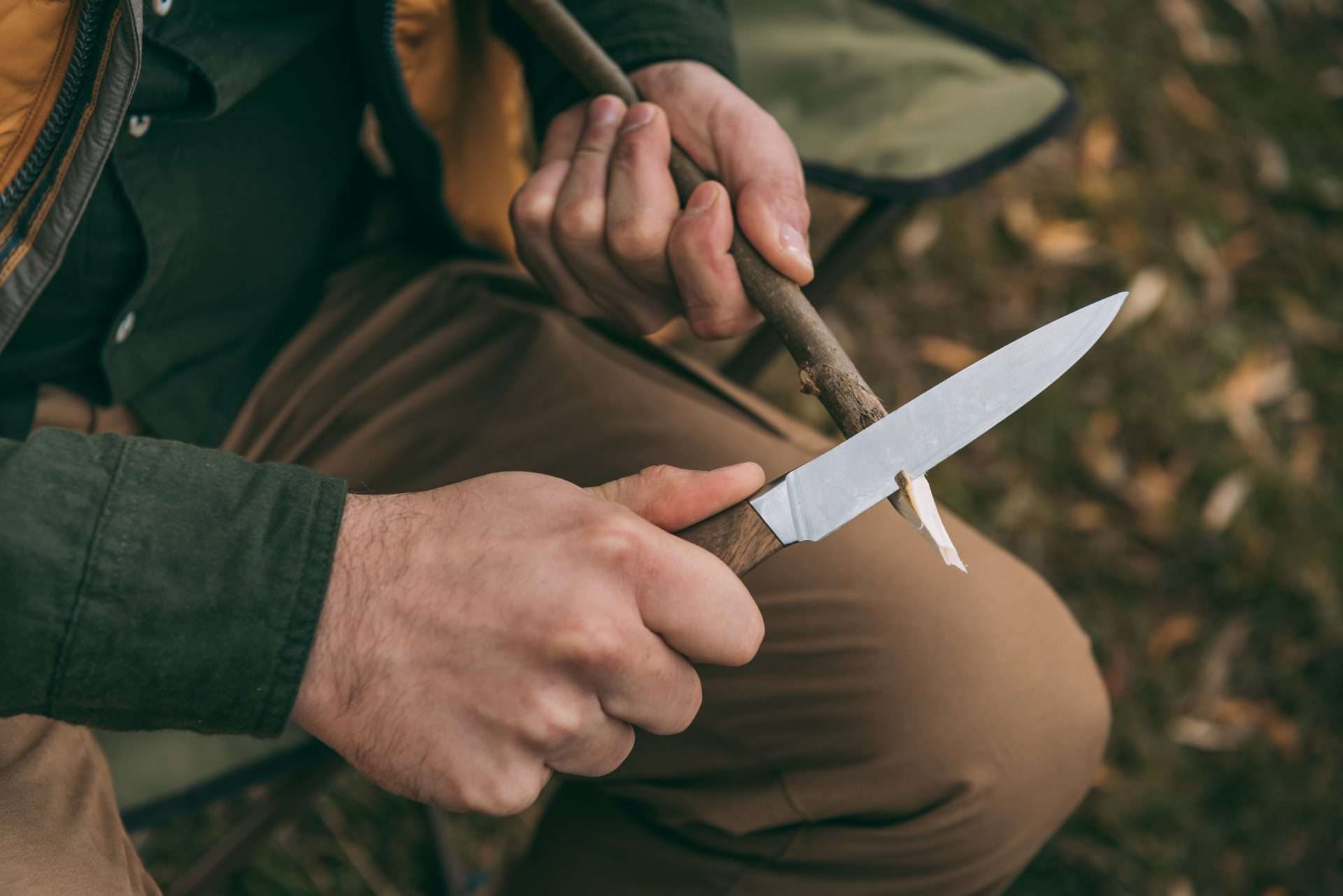 Man using survival knife to whittle stick.
