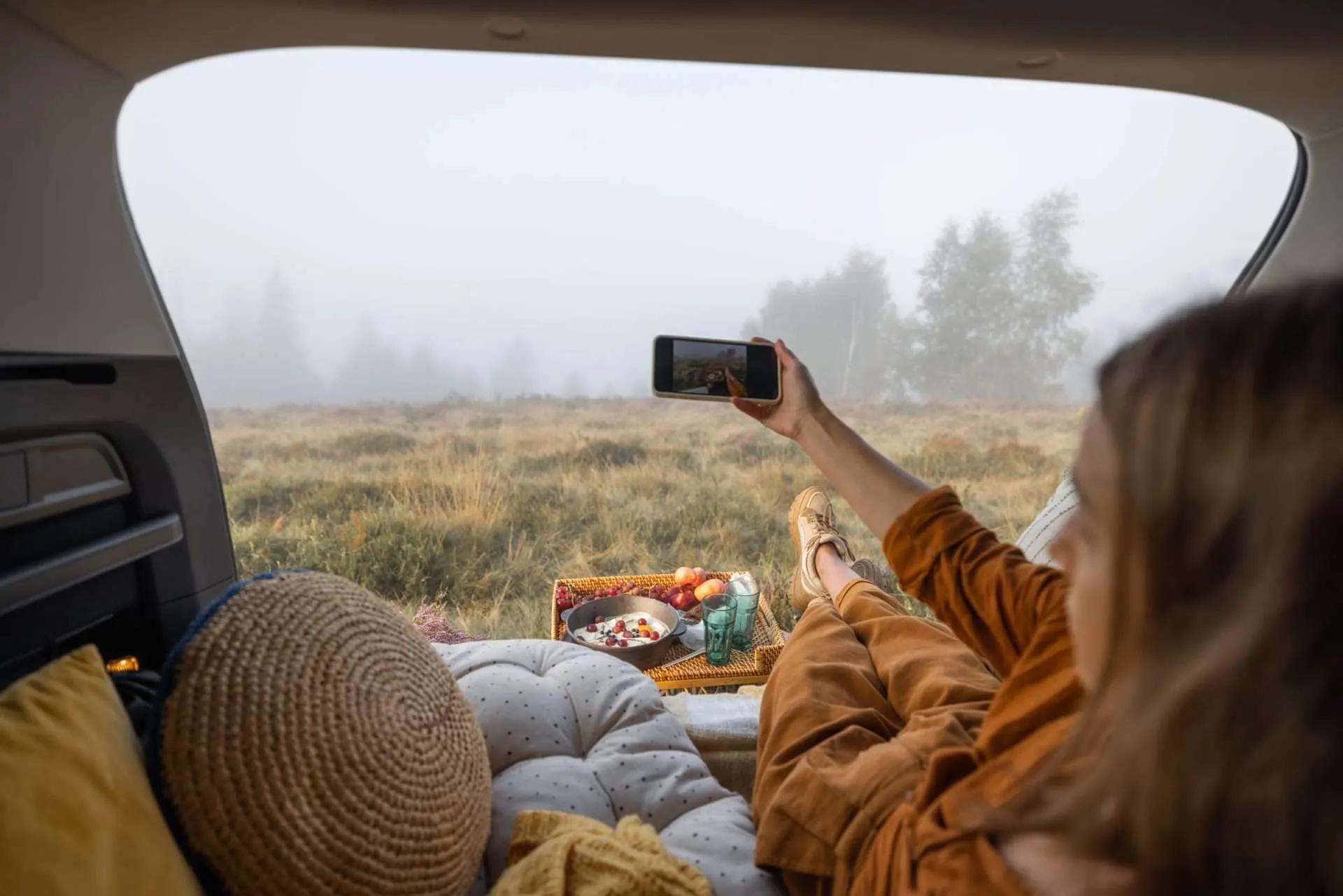 Woman taking photo while laying in bed in the back of her car.