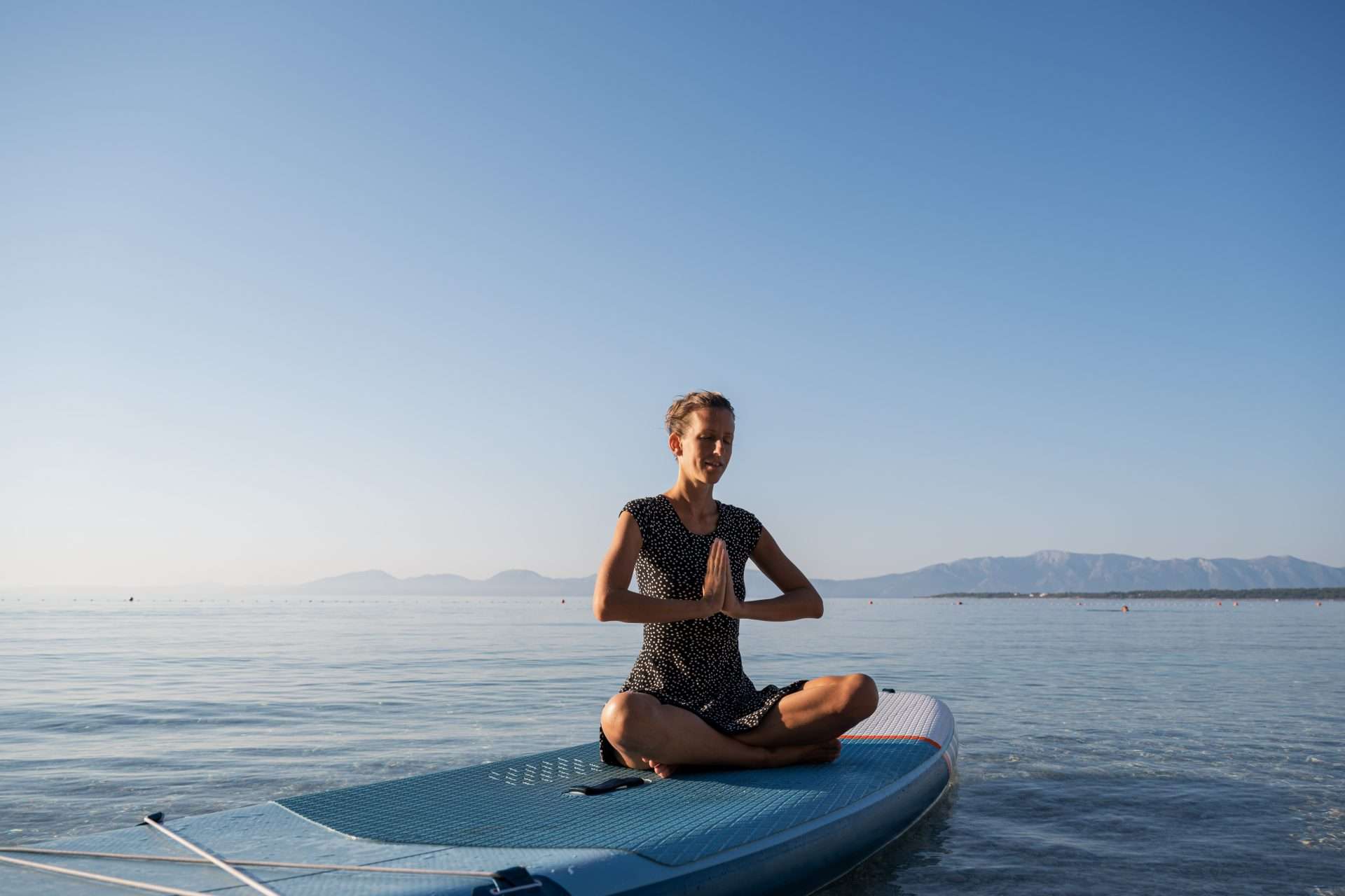 Woman meditating on top of paddle board in ocean.