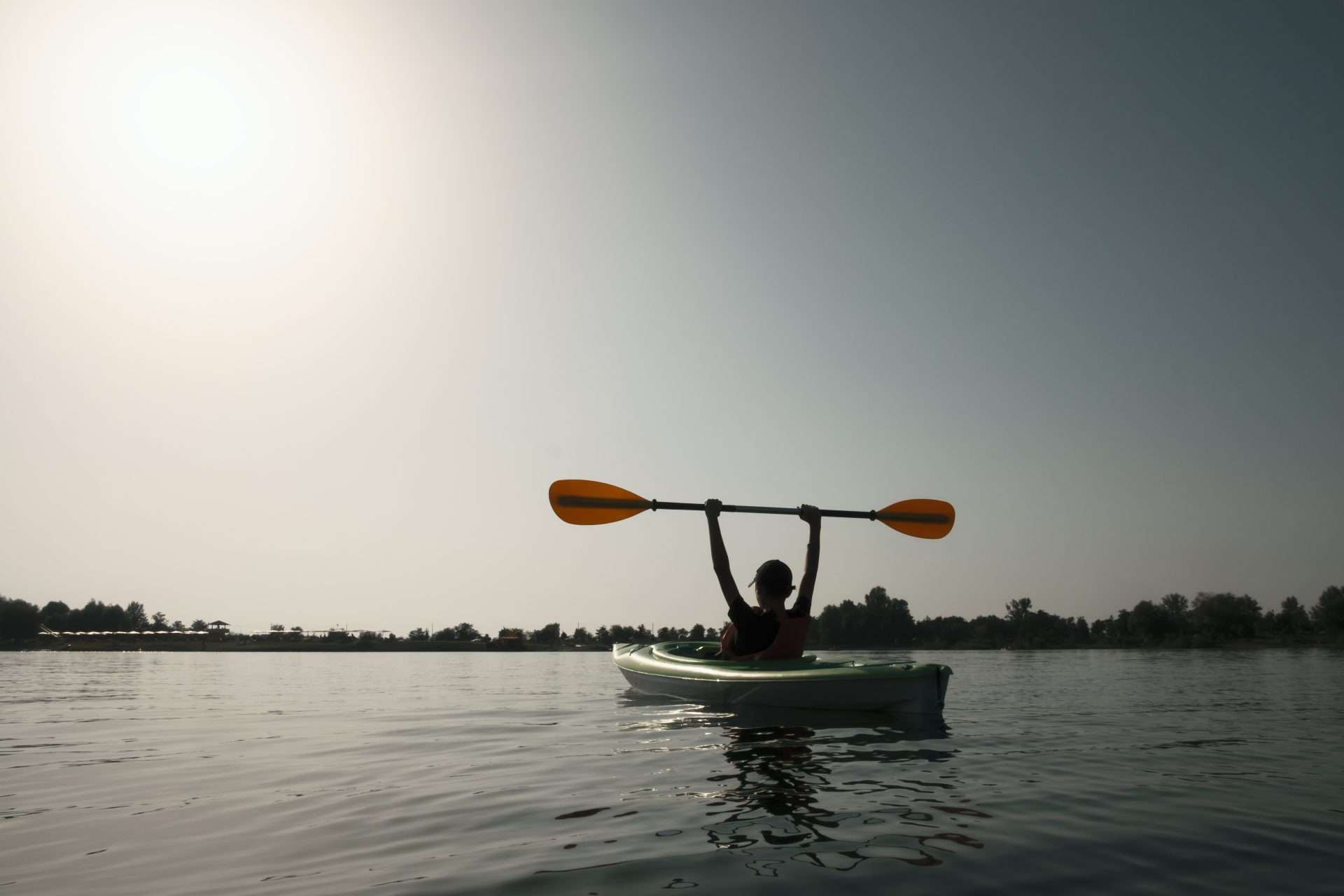 Boy sitting in kayak holding up oars proudly.
