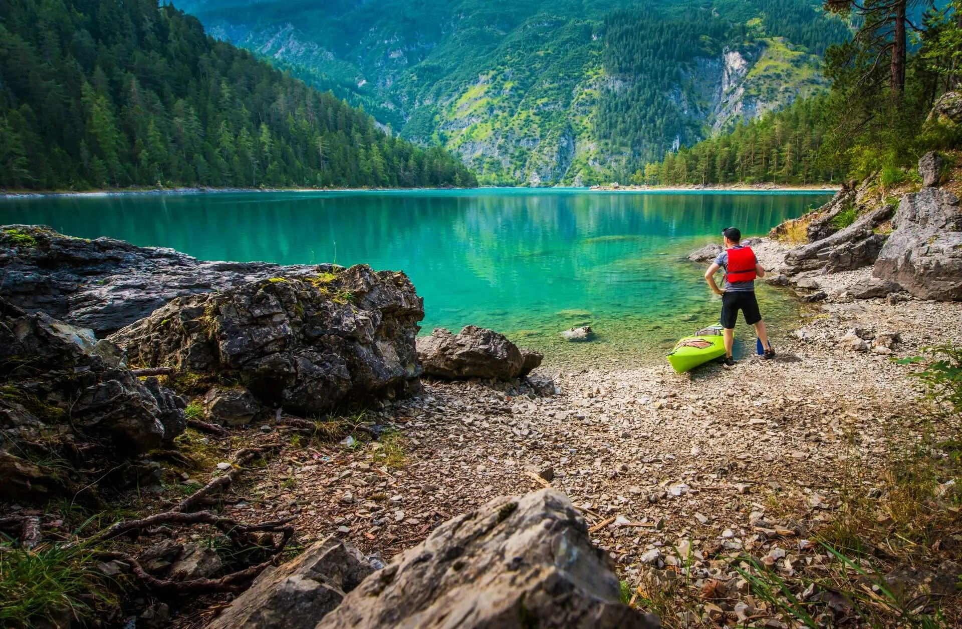 Camper standing next to kayak along stunning lake