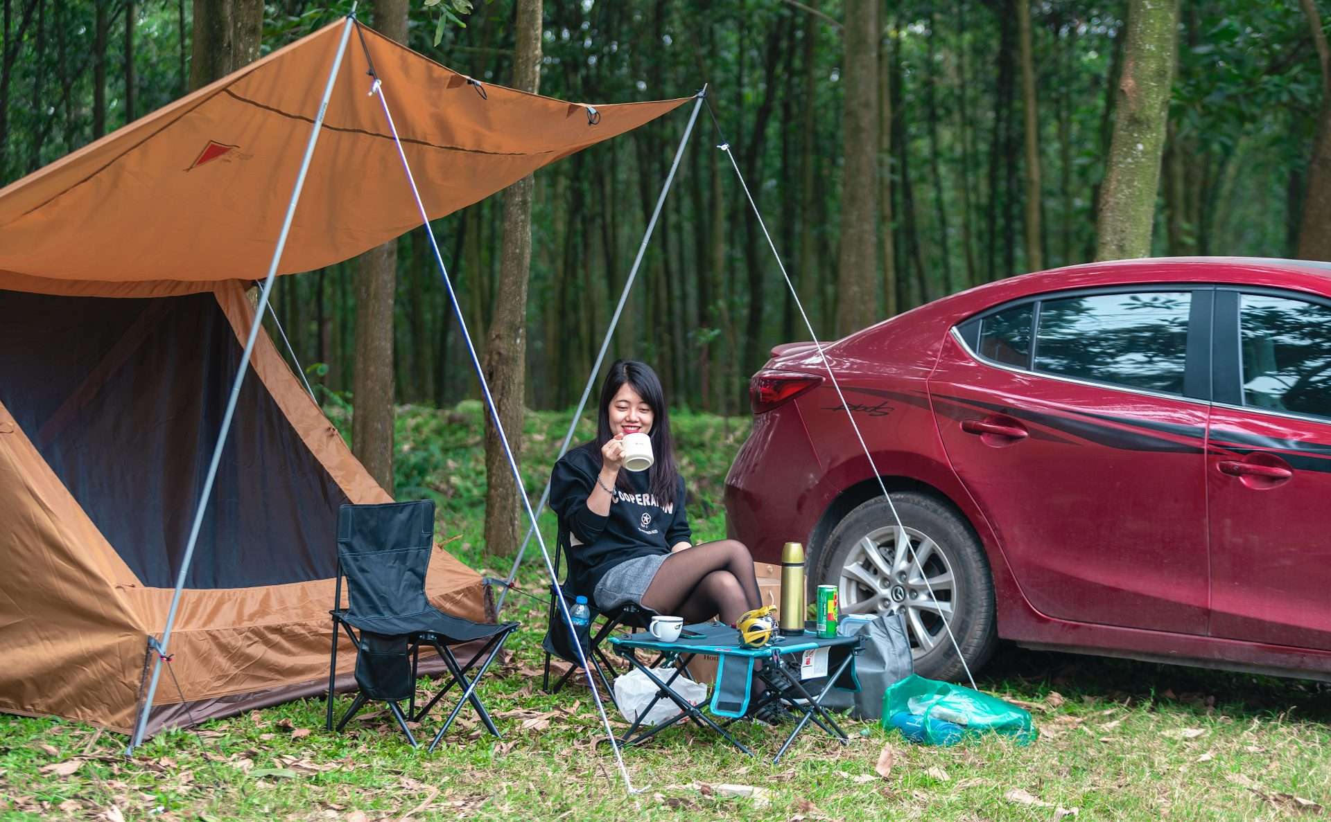 Woman drinking coffee next to car and tent while camping on BLM land