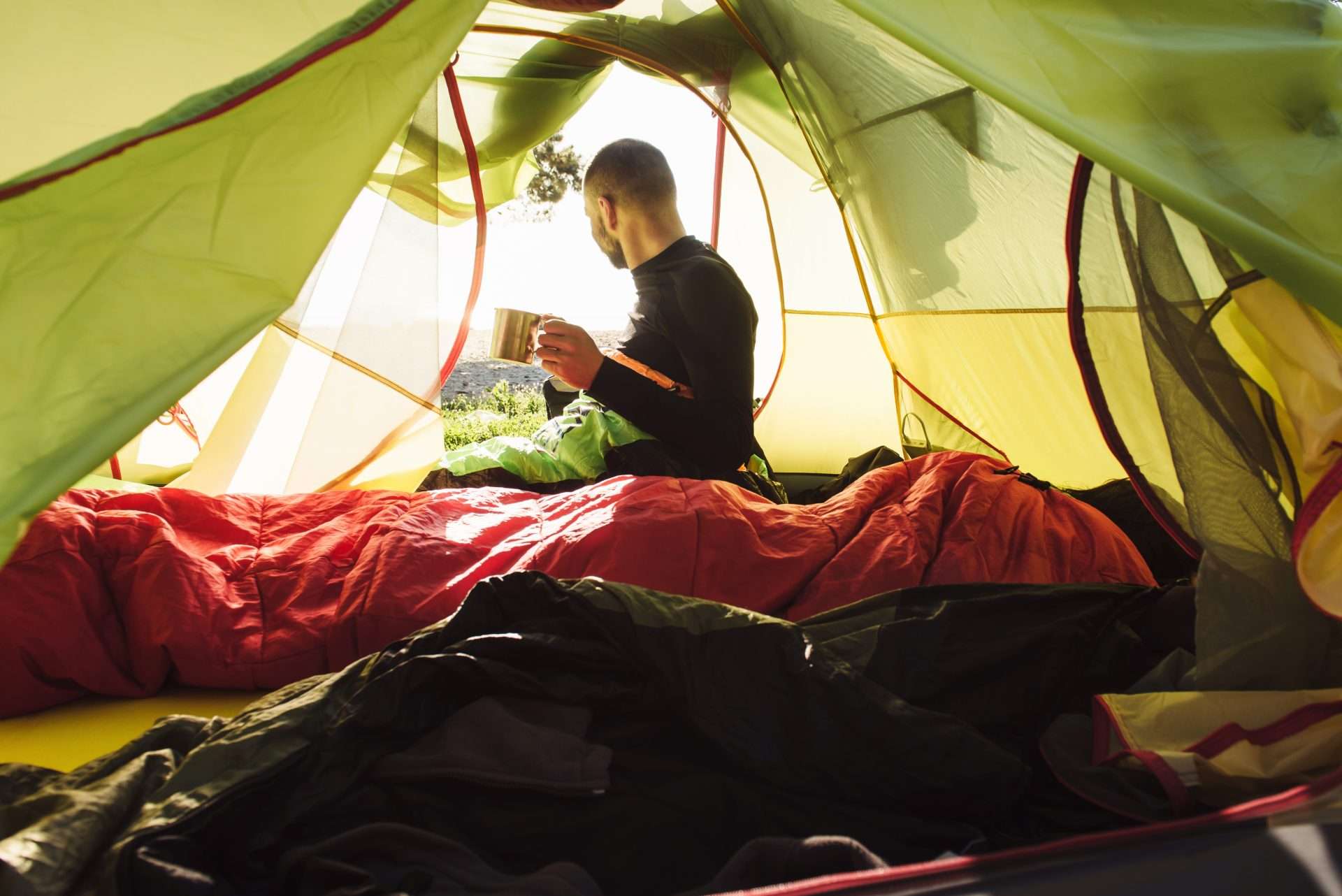 Man sitting in sleeping bag inside tent while using